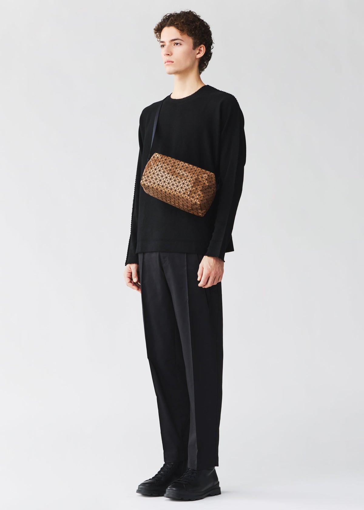 A model wears the BAO BAO ISSEY MIYAKE SADDLE BAG REFLECTOR saddle-bag-reflector-shoulder-bag-copper-brown.