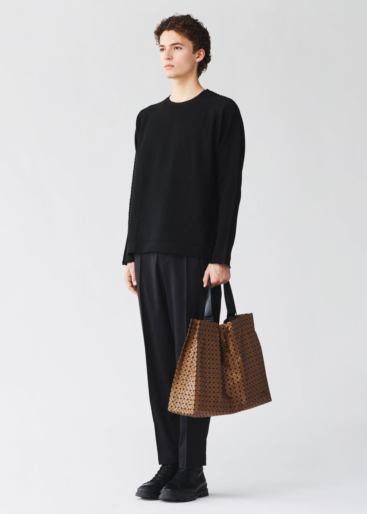 A model wears the BAO BAO ISSEY MIYAKE CART REFLECTOR cart-reflector-tote-bag-copper-brown.