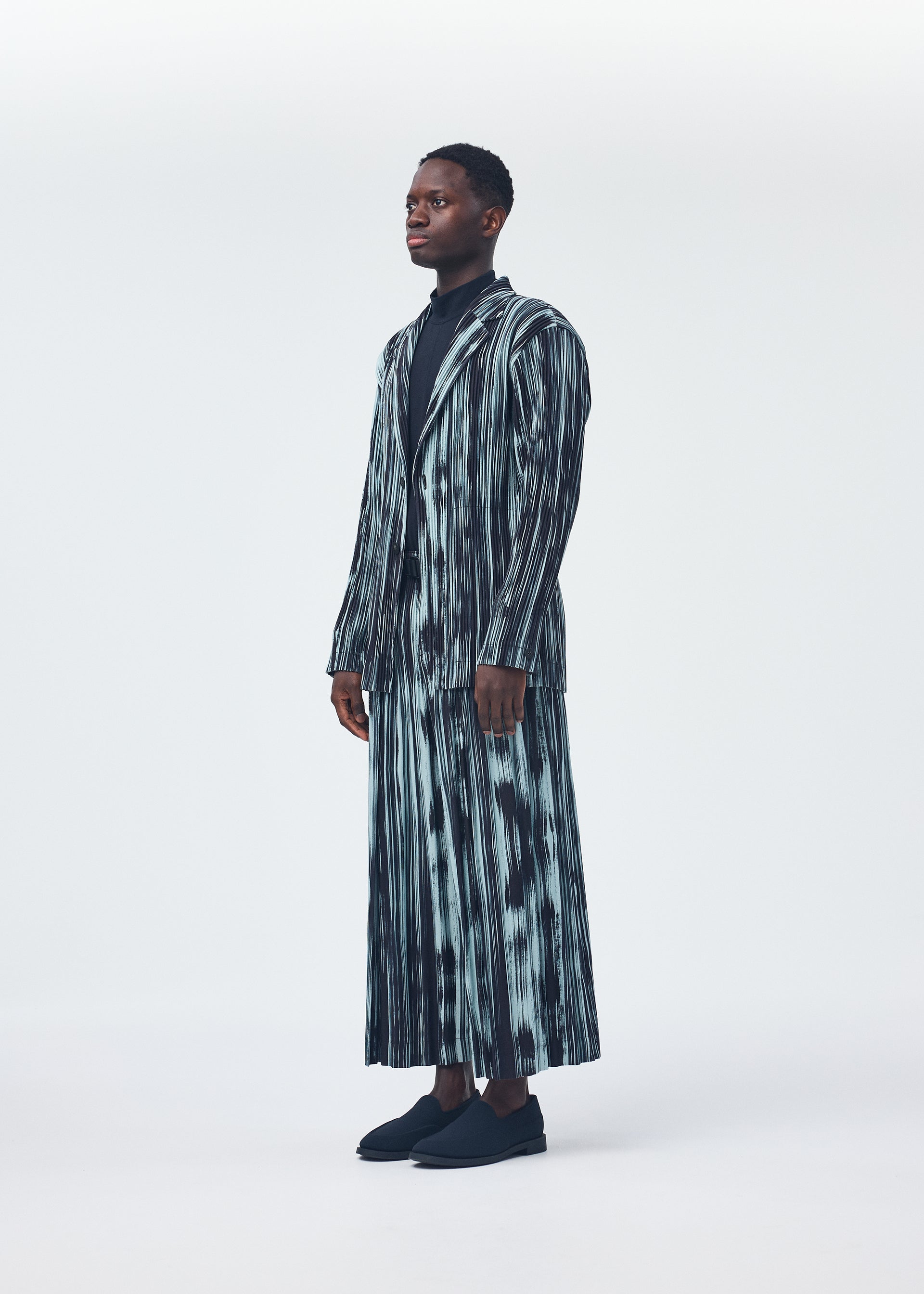 A model wears the HOMME PLISSÉ ISSEY MIYAKE BRUSHSTROKE STRIPE trousers.