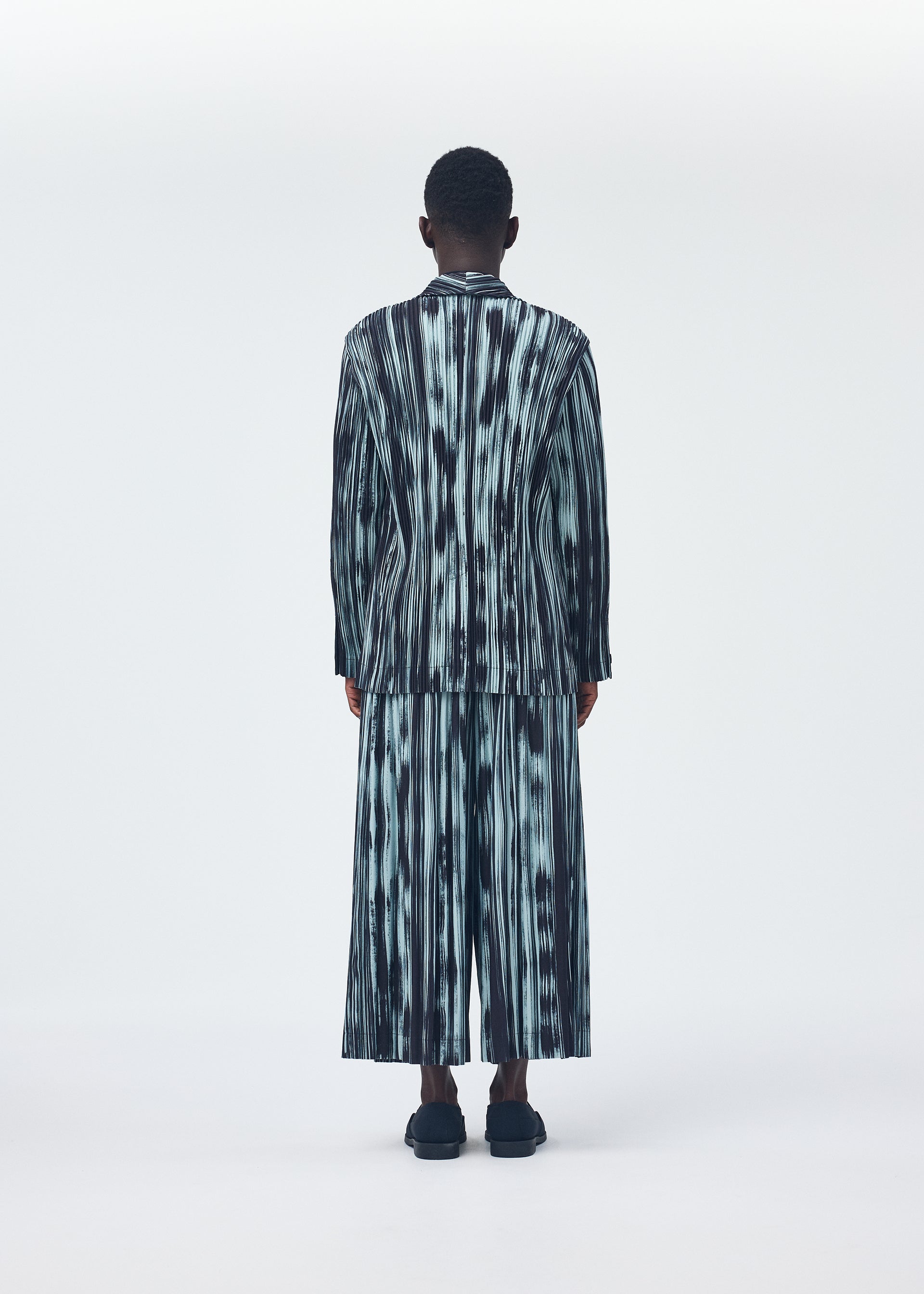 A model wears the HOMME PLISSÉ ISSEY MIYAKE BRUSHSTROKE STRIPE trousers.