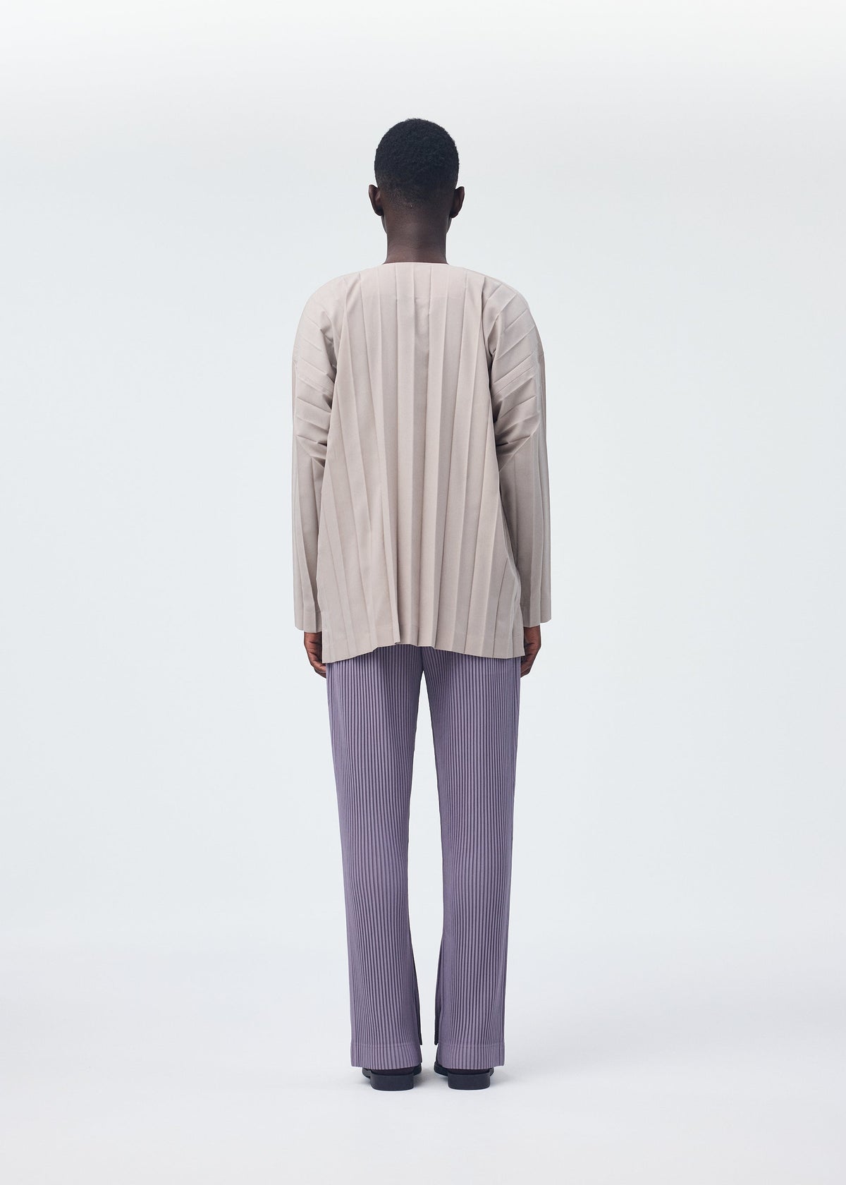 A model wears the HOMME PLISSÉ ISSEY MIYAKE PLEATS BOTTOMS 1 trousers.