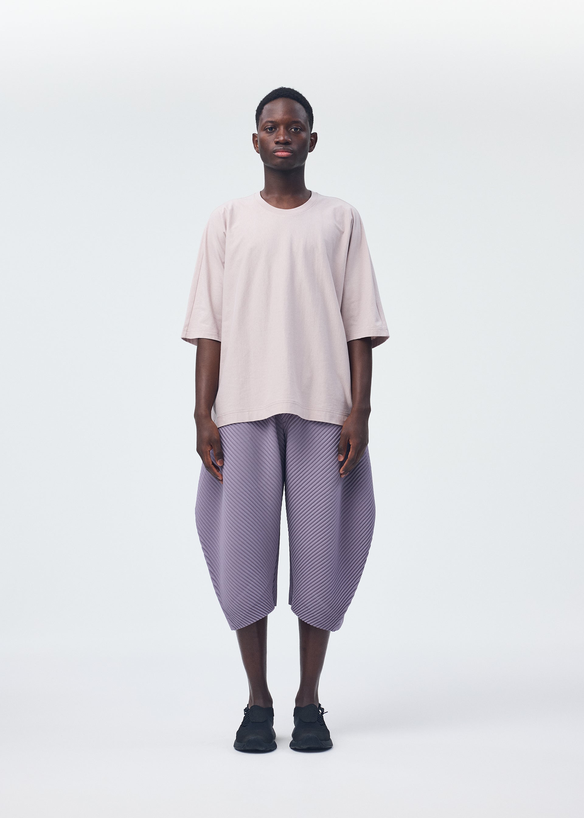 A model wears the HOMME PLISSÉ ISSEY MIYAKE PLEATS BOTTOMS 1 trousers.