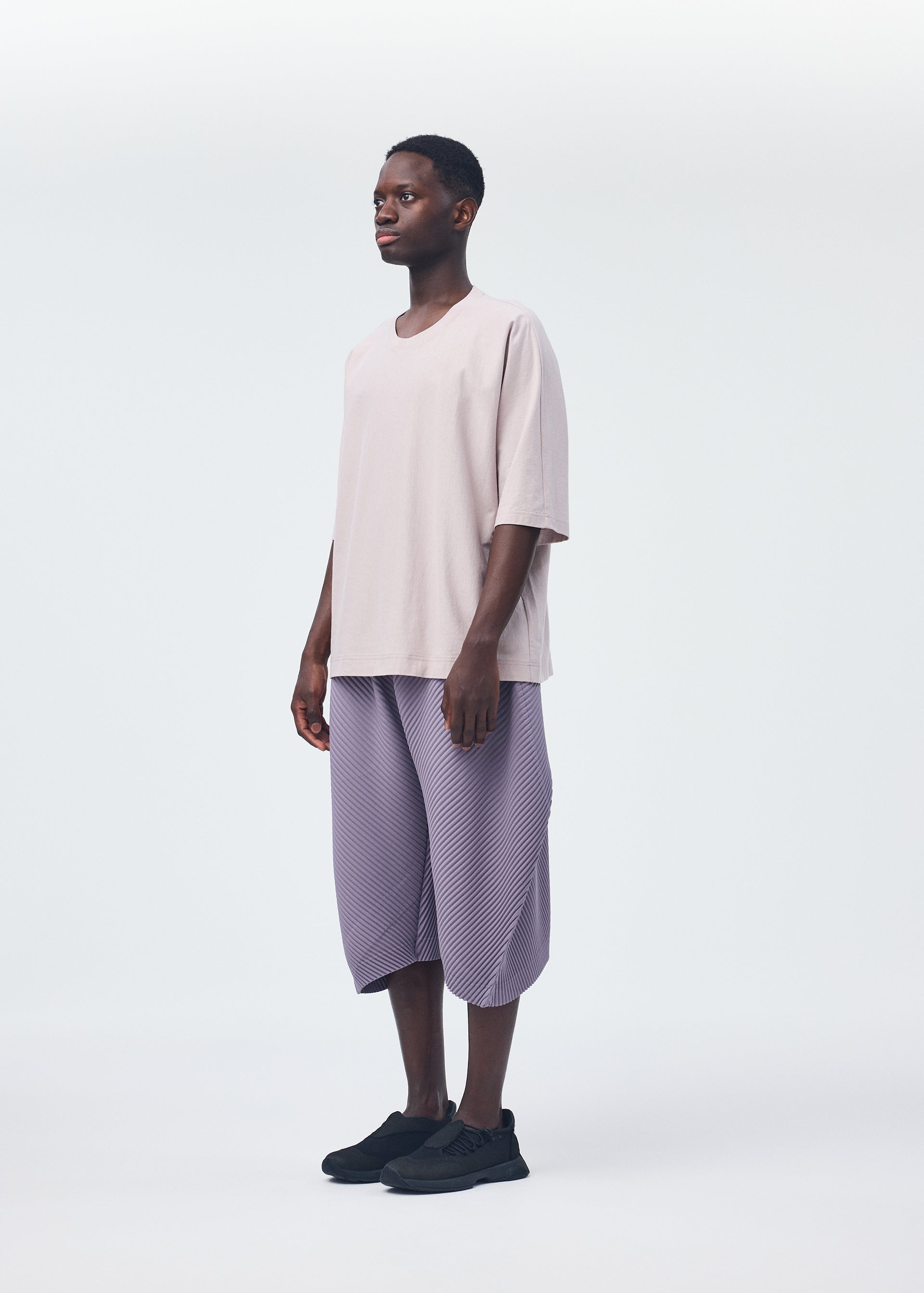A model wears the HOMME PLISSÉ ISSEY MIYAKE PLEATS BOTTOMS 1 trousers.