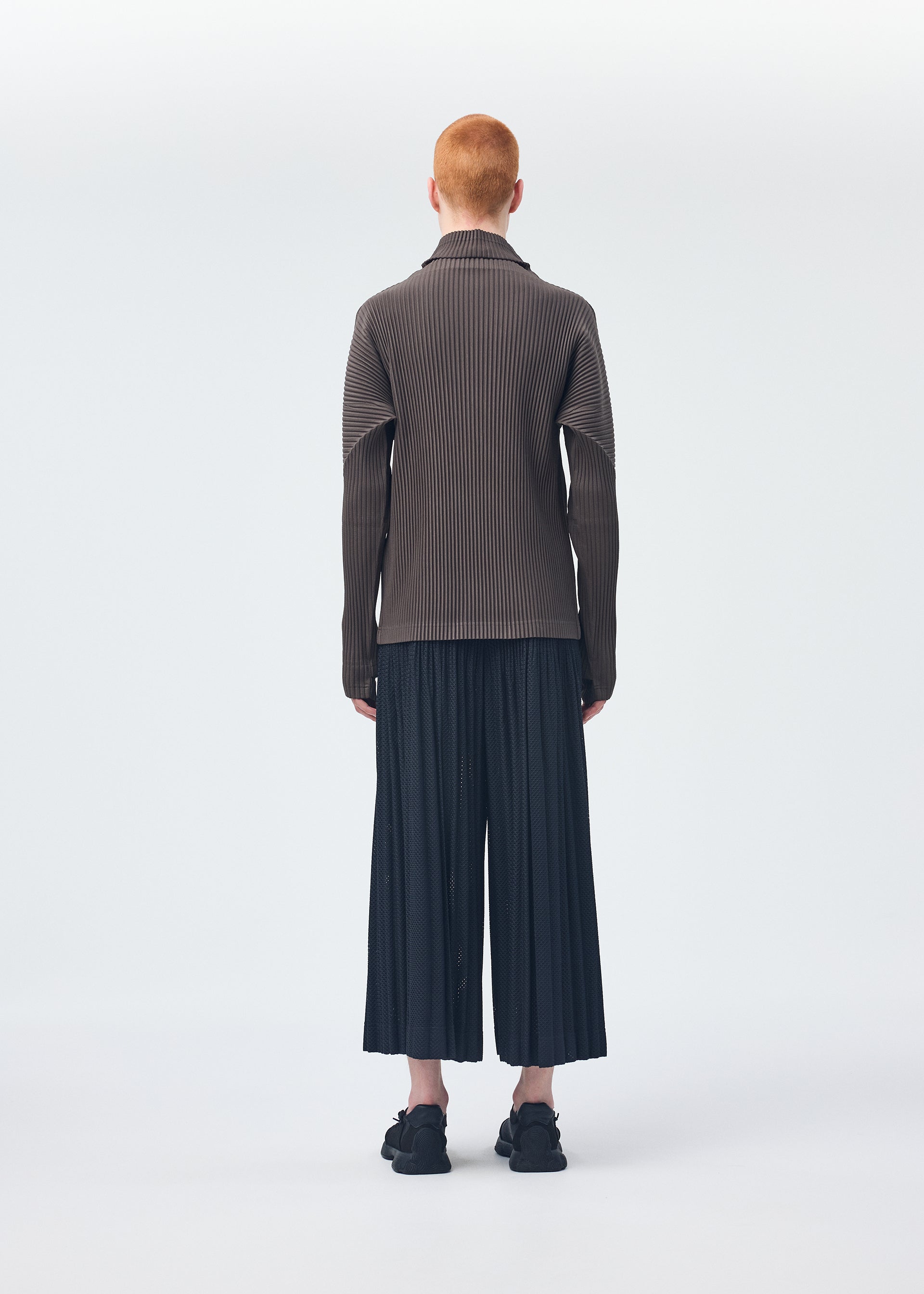 A model wears the Homme Plisse Issey Miyake WICKERWORK MESH trousers.