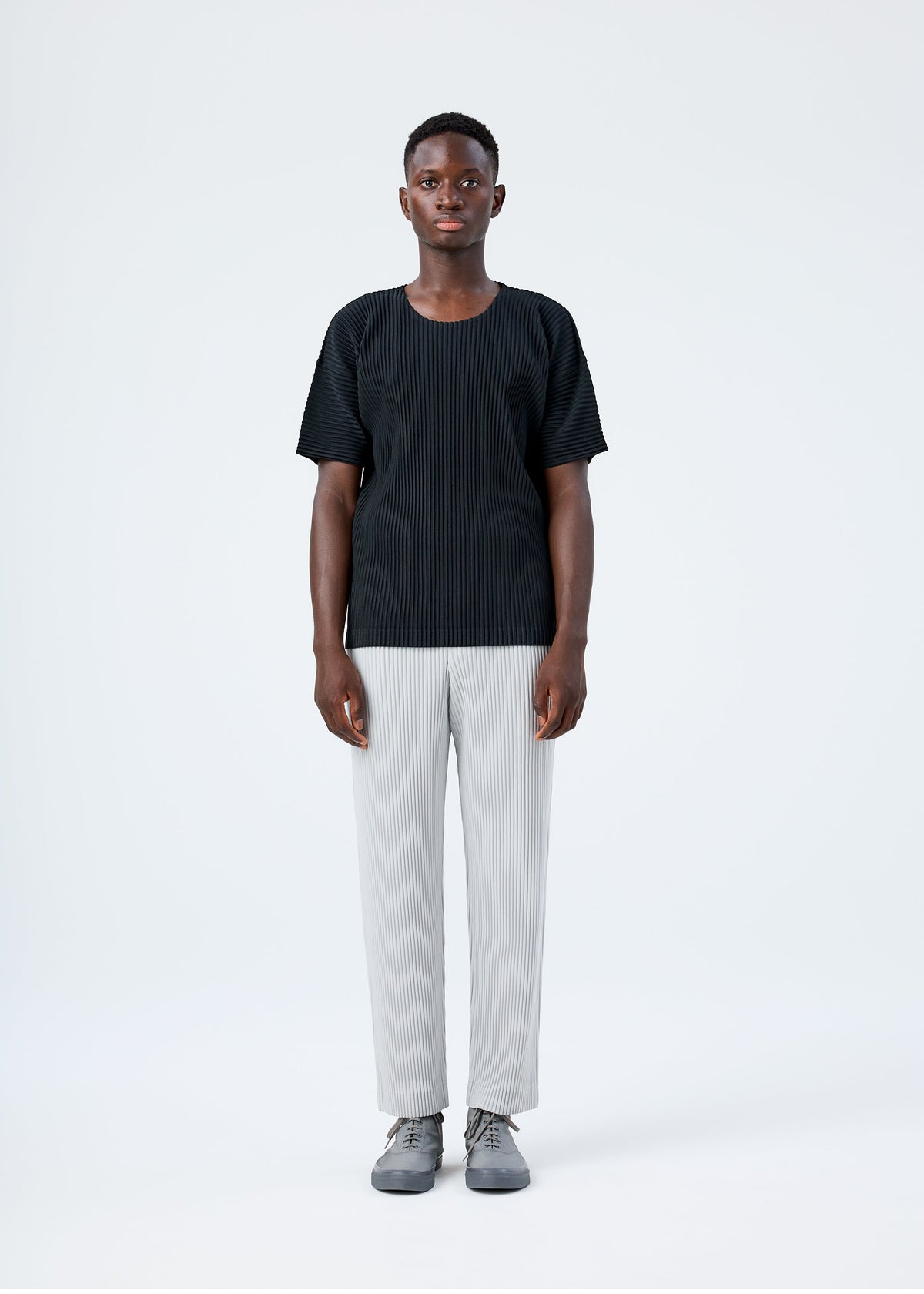 A model wears the HOMME PLISSÉ ISSEY MIYAKE BASICS basics-trousers-navy-2-fw26.