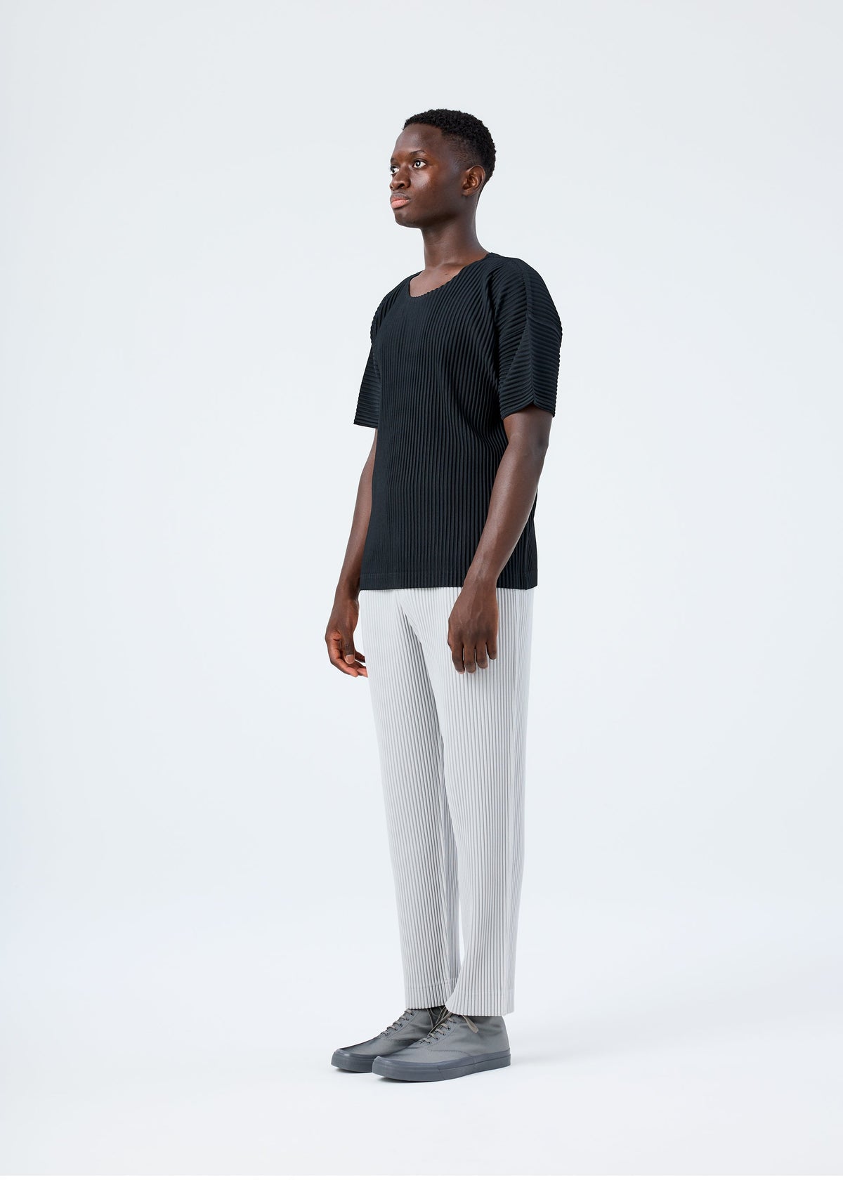 A model wears the HOMME PLISSÉ ISSEY MIYAKE BASICS basics-trousers-navy-2-fw26.