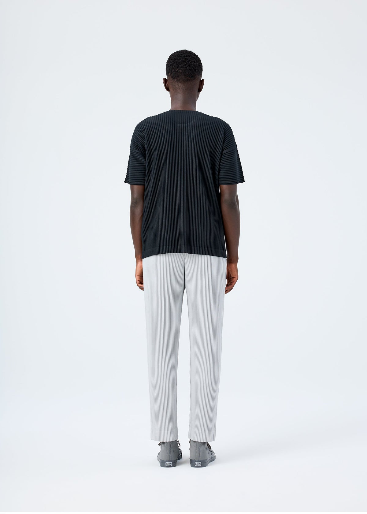 A model wears the HOMME PLISSÉ ISSEY MIYAKE BASICS basics-trousers-black-1-fw26.