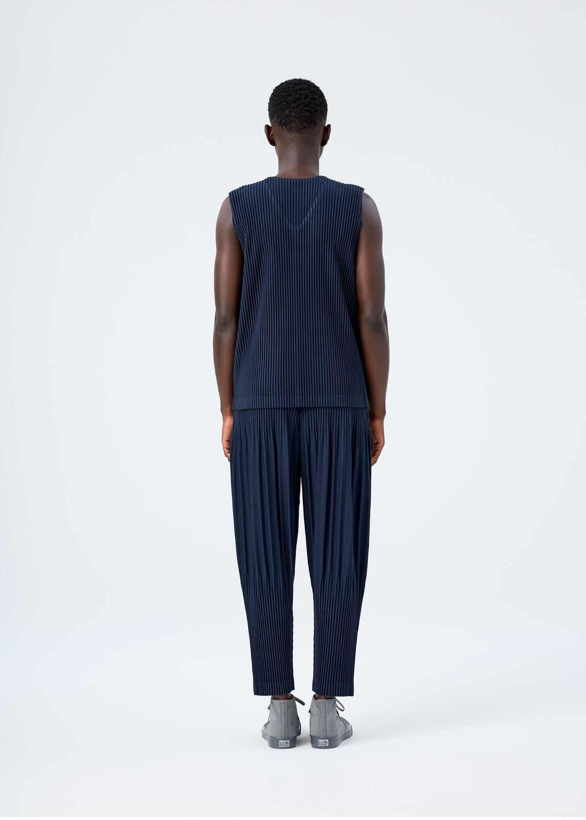 A model wears the HOMME PLISSÉ ISSEY MIYAKE BASICS basics-trousers-light-grey-3.