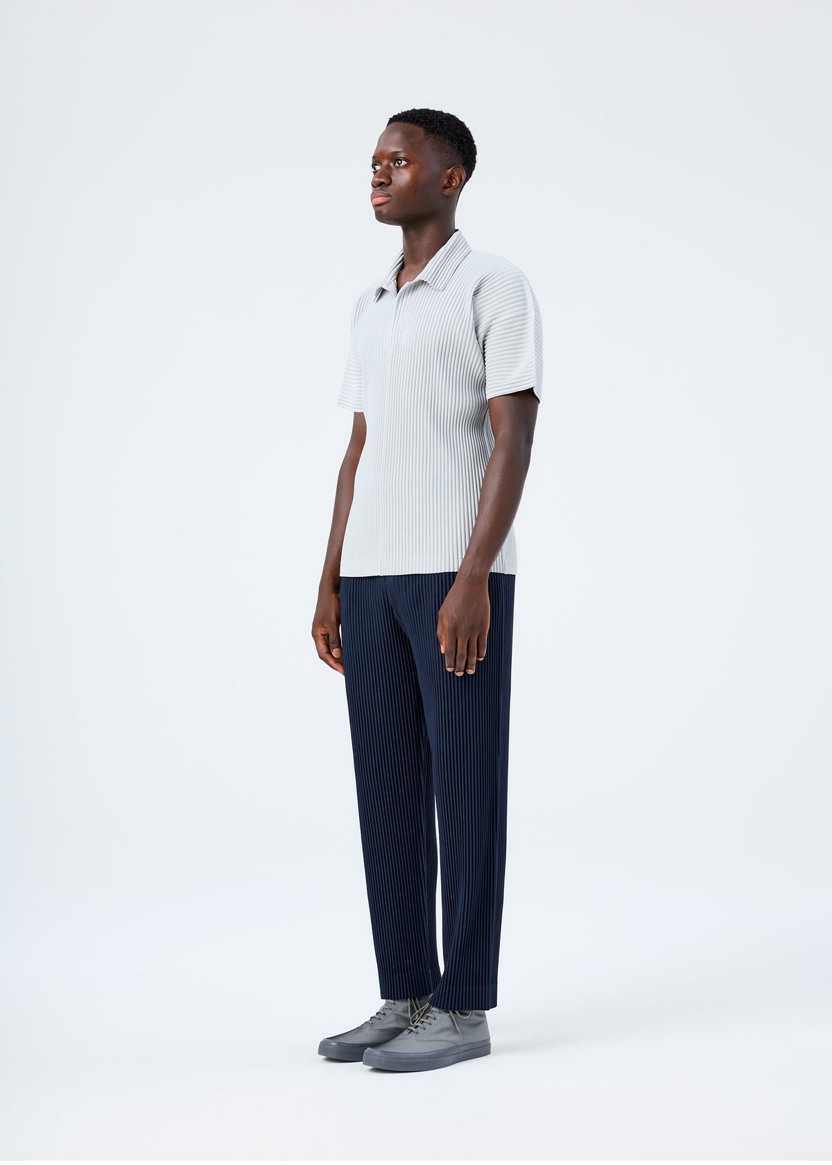 A model wears the HOMME PLISSÉ ISSEY MIYAKE BASICS basics-polo-shirt-black-fw26.