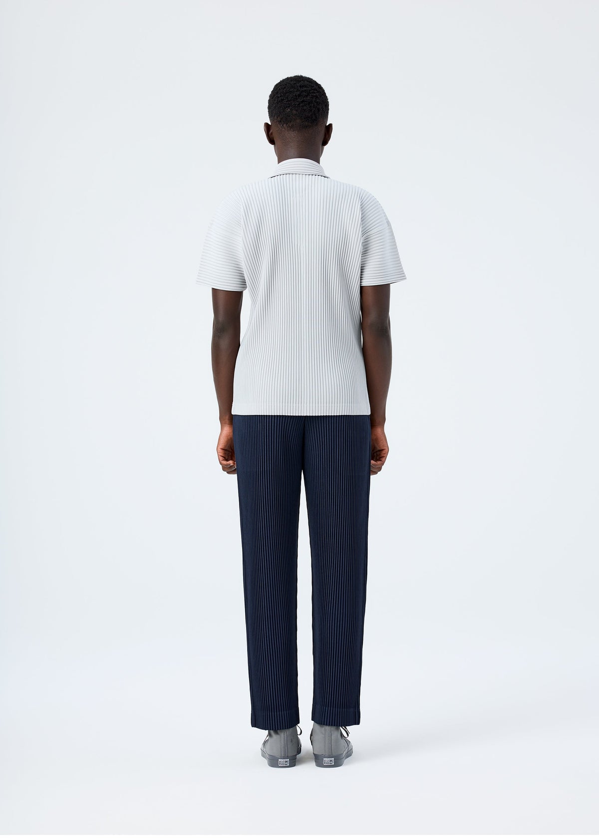 A model wears the HOMME PLISSÉ ISSEY MIYAKE BASICS basics-polo-shirt-black-fw26.