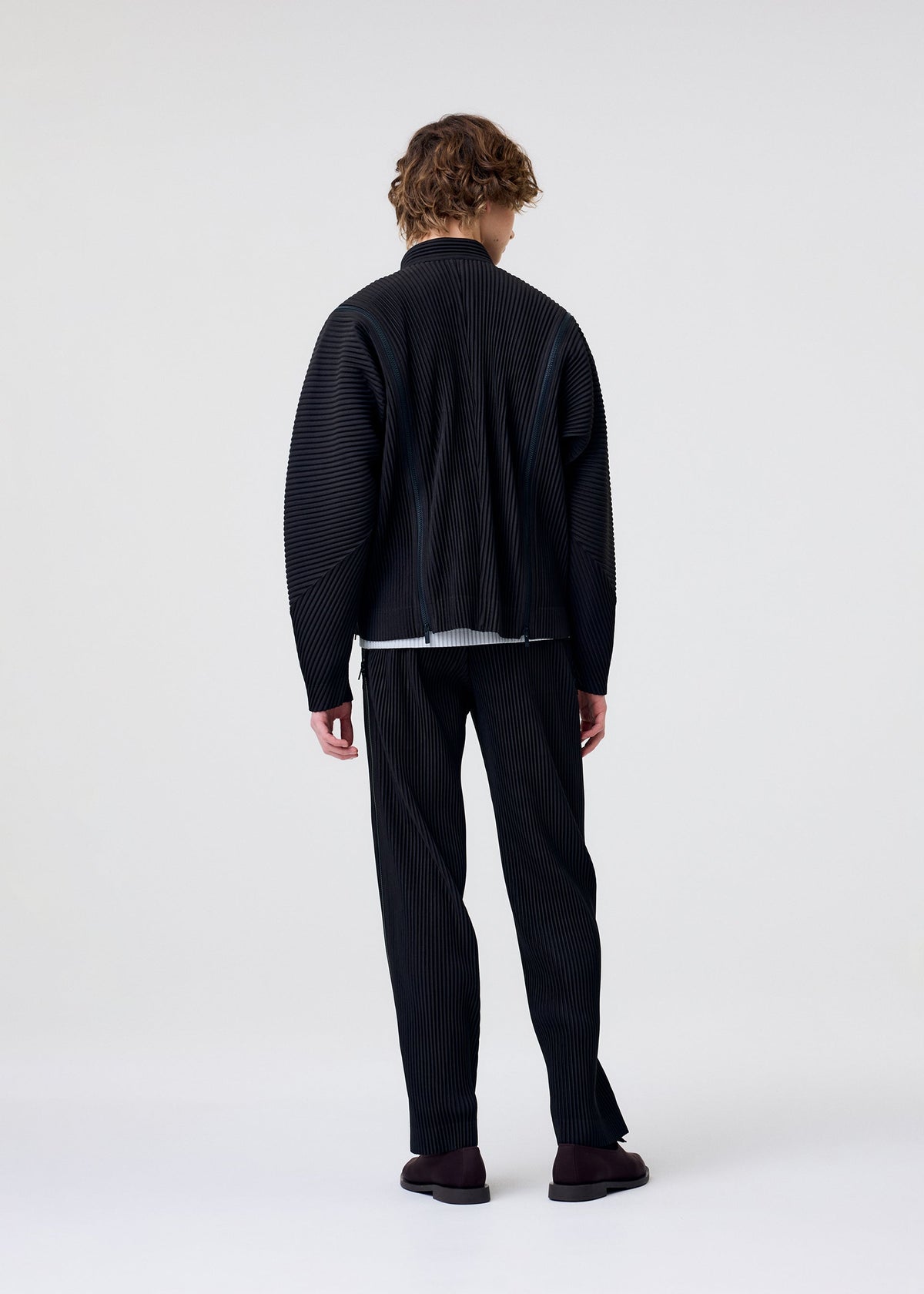 A model wears the HOMME PLISSÉ ISSEY MIYAKE MULTI-FASTENED multi-fastened-blouson-lucca-storico-blue.