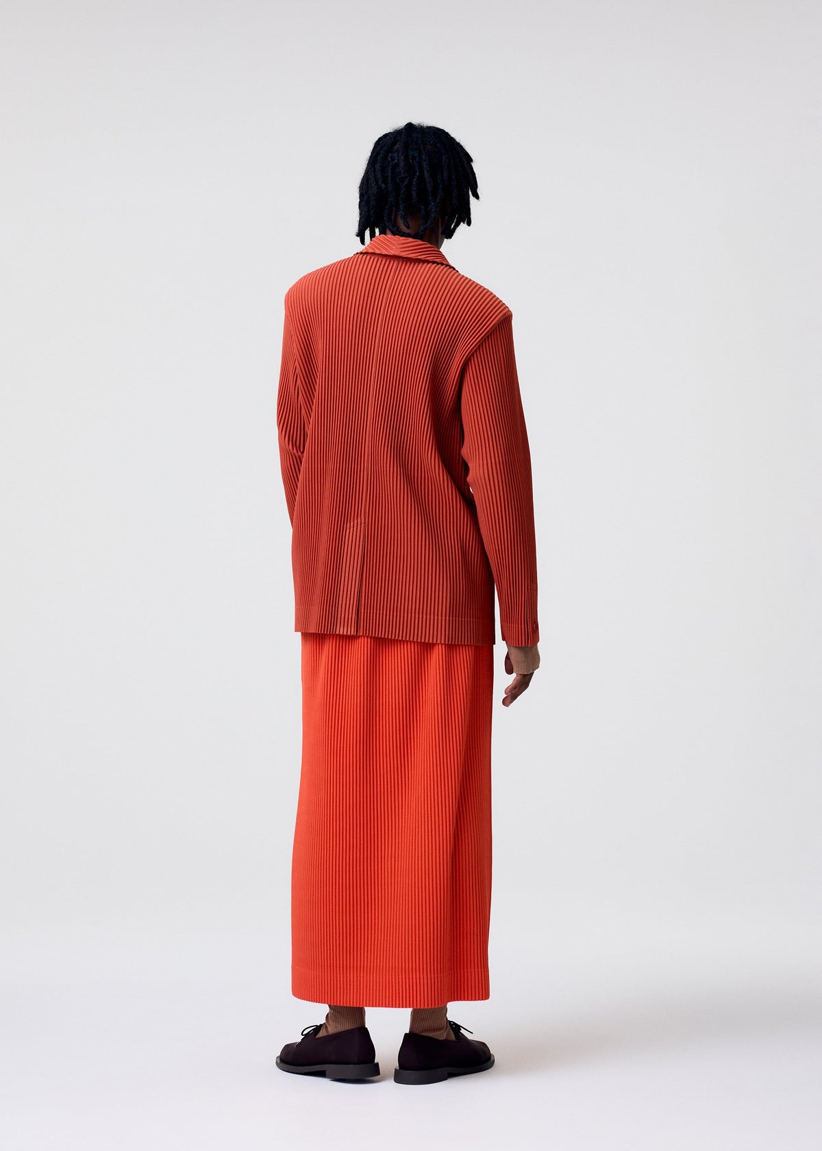 A model wears the HOMME PLISSÉ ISSEY MIYAKE TAILORED PLEATS 3 tailored-pleats-3-jacket-genova-metal-ochre.