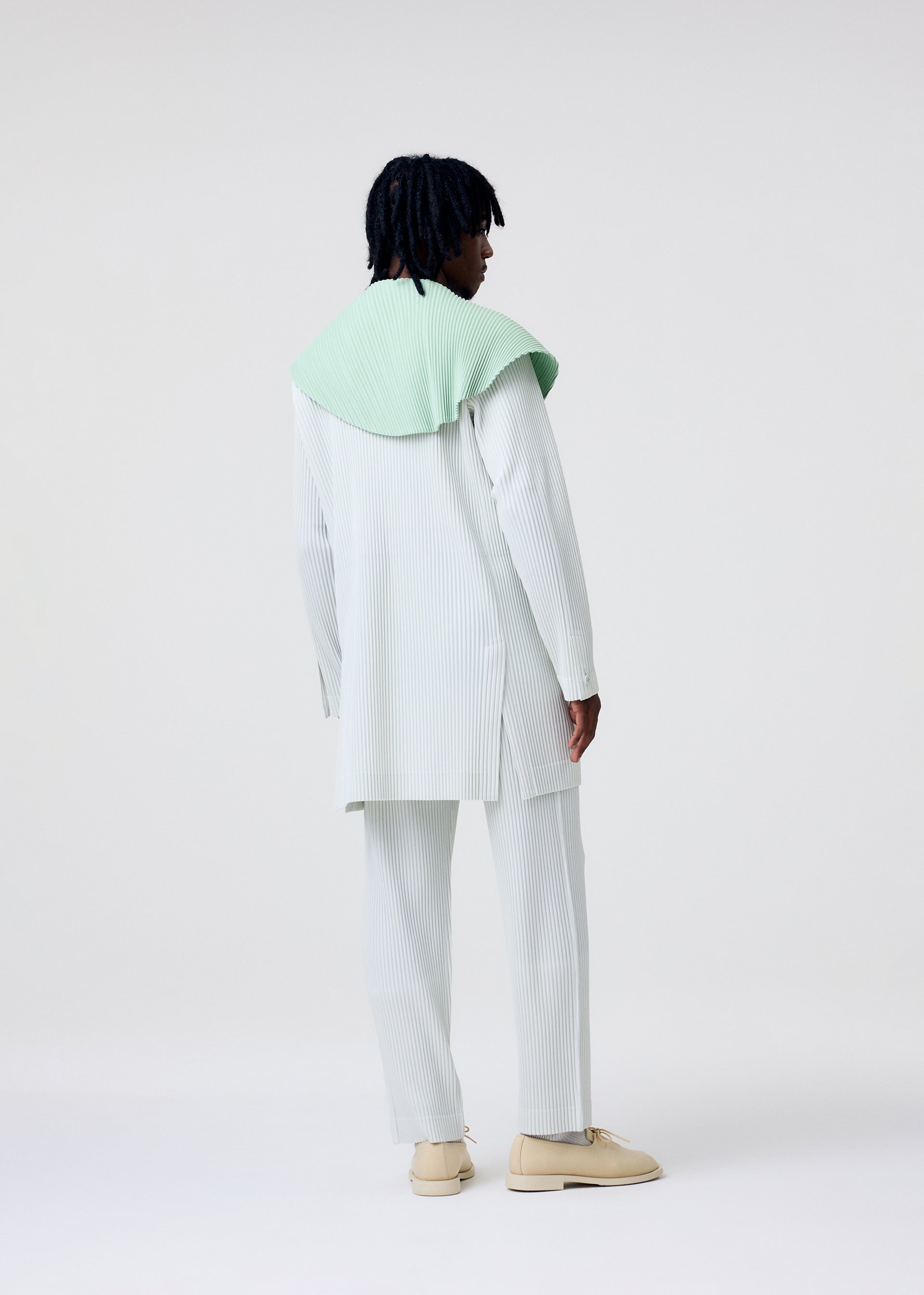 A model wears the HOMME PLISSÉ ISSEY MIYAKE TAILORED PLEATS 3 tailored-pleats-3-jacket-genova-metal-ochre-1.