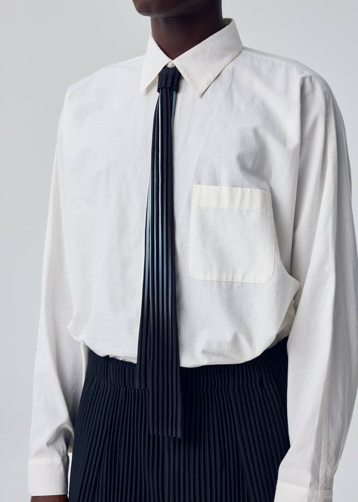 A model wears the HOMME PLISSÉ ISSEY MIYAKE IN THE SHADOW PLEATS TIE tie.