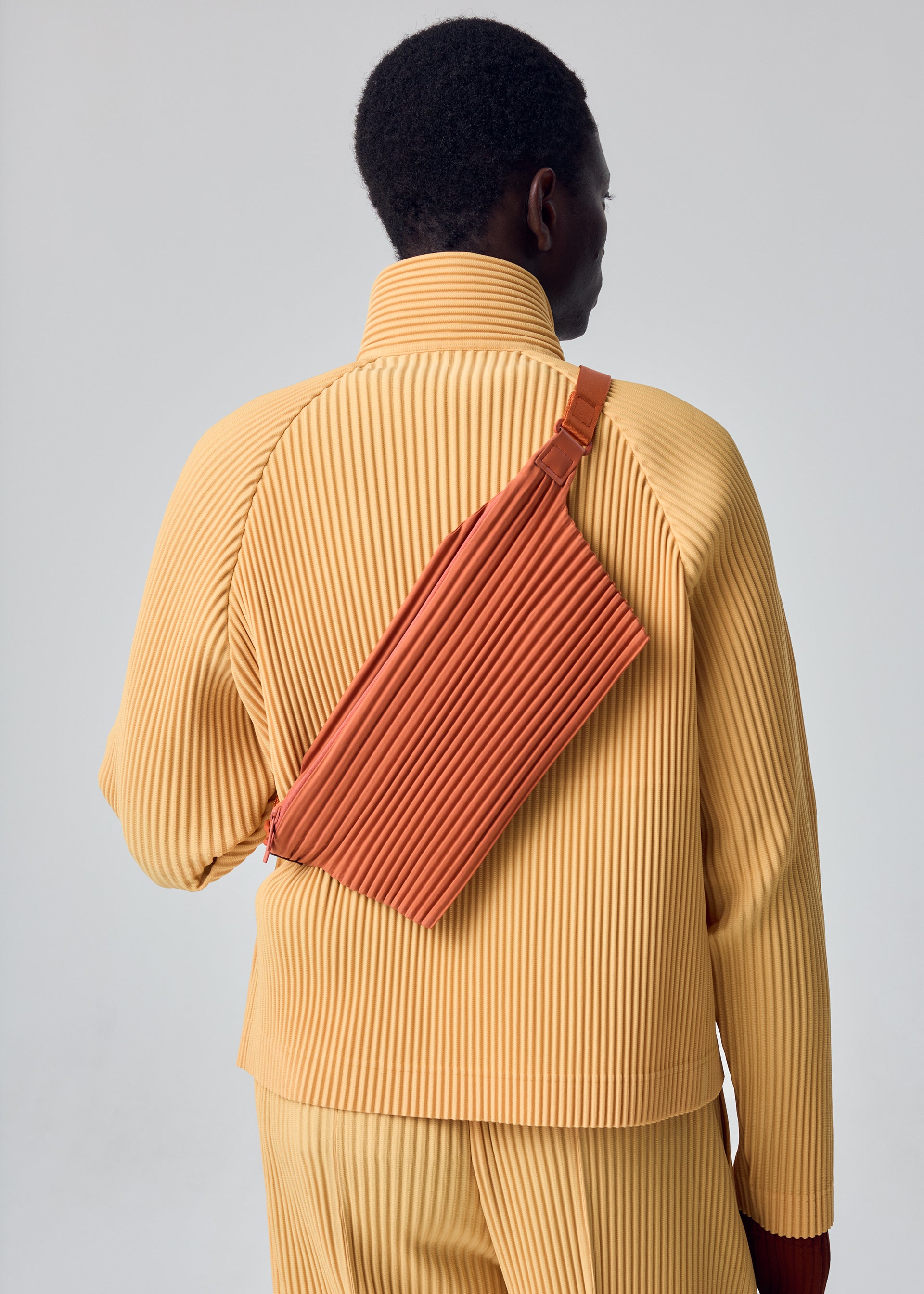 A model wears the HOMME PLISSÉ ISSEY MIYAKE PLEATS SLIM BAG pleats-slim-bag-bag-black-1.