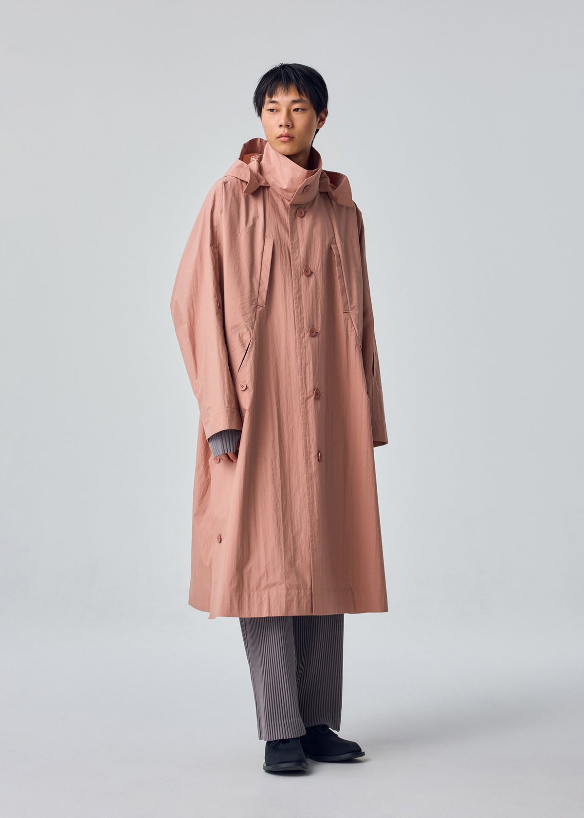 A model wears the HOMME PLISSÉ ISSEY MIYAKE SLIT COAT coat.