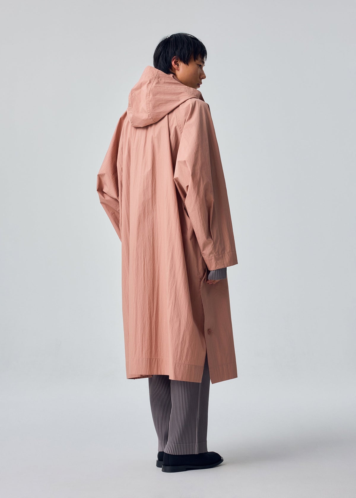 A model wears the HOMME PLISSÉ ISSEY MIYAKE SLIT COAT coat.