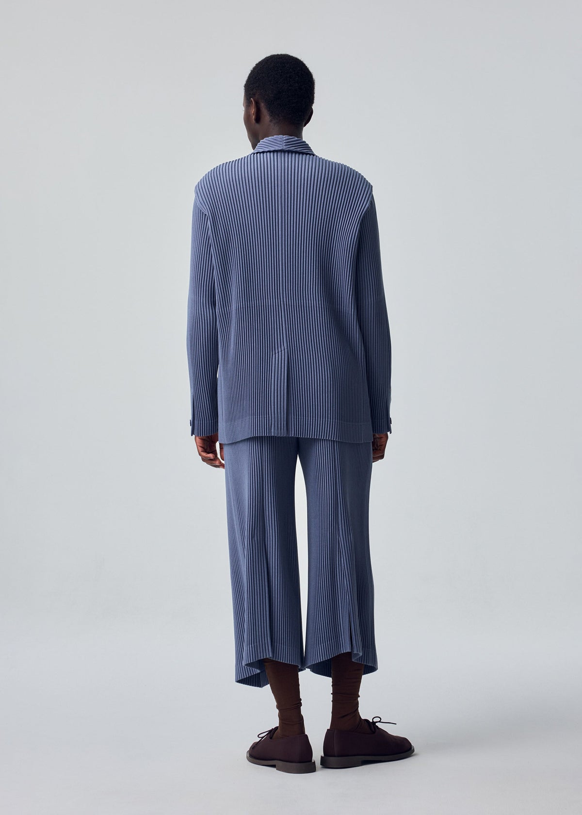 A model wears the HOMME PLISSÉ ISSEY MIYAKE KERSEY PLEATS trousers.