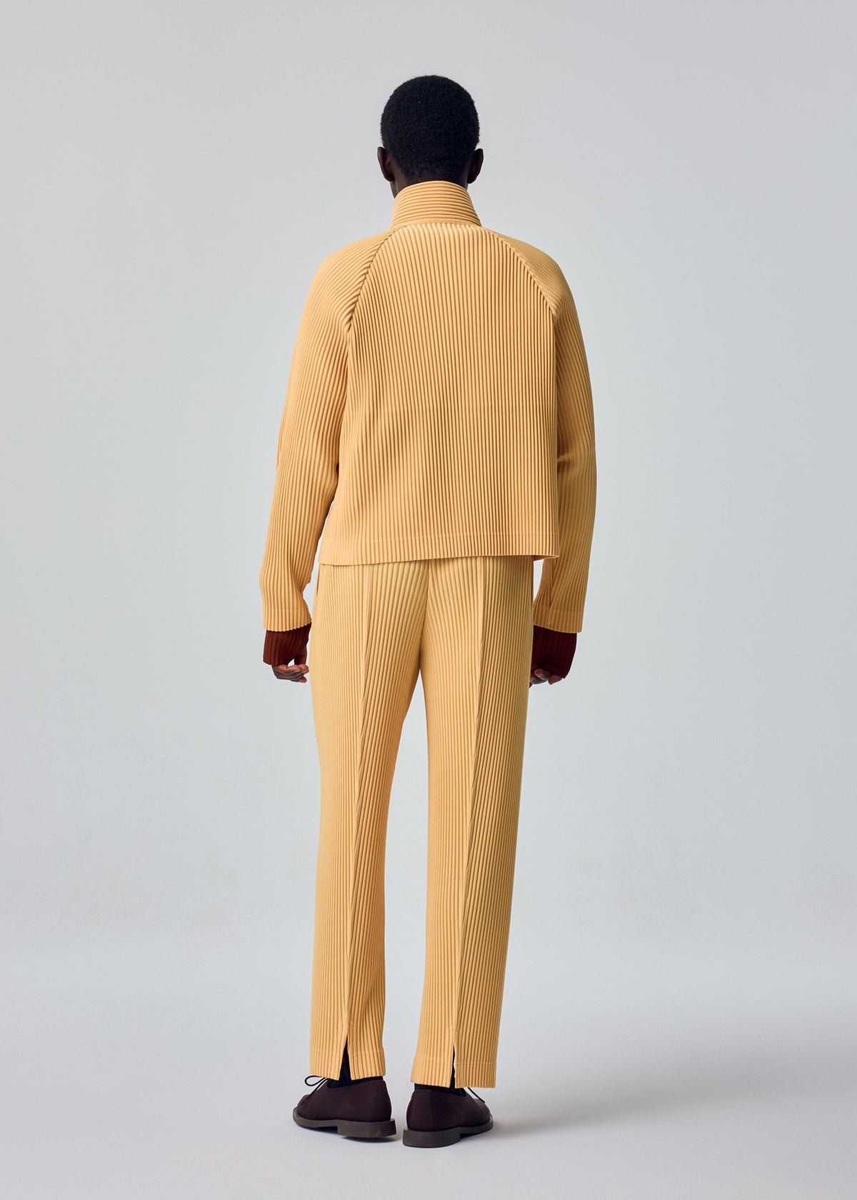 A model wears the HOMME PLISSÉ ISSEY MIYAKE TAILORED PLEATS 1 tailored-pleats-1-blouson-shadow-brown.