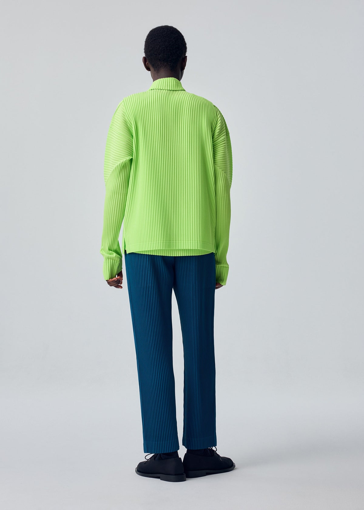 A model wears the HOMME PLISSÉ ISSEY MIYAKE TAILORED PLEATS 1 tailored-pleats-1-trousers-glow-orange.