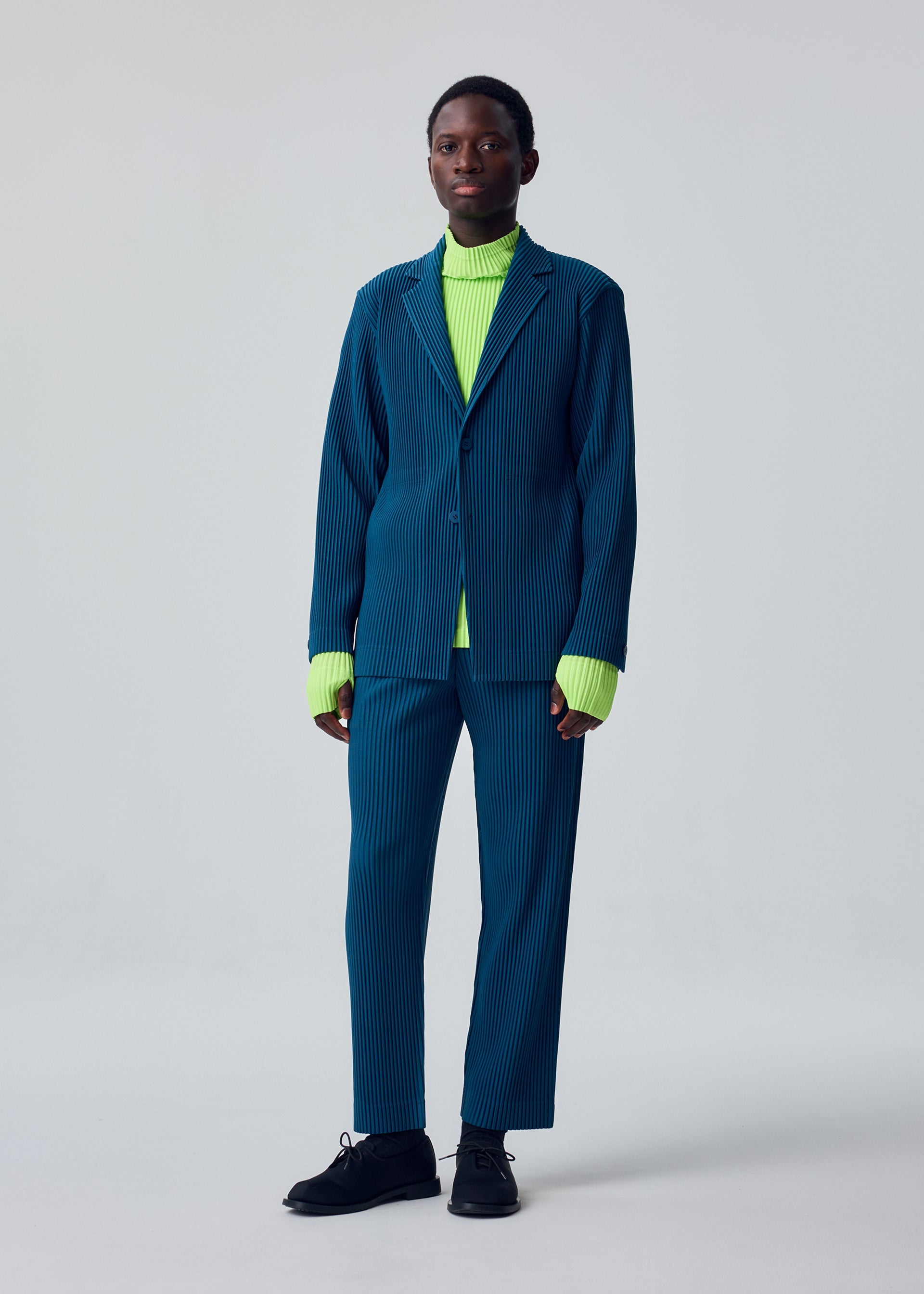 A model wears the HOMME PLISSÉ ISSEY MIYAKE TAILORED PLEATS 1 tailored-pleats-1-trousers-glow-orange.