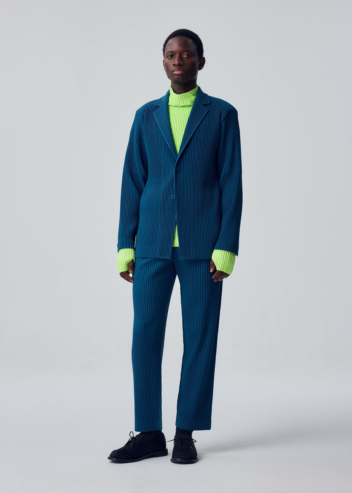 A model wears the HOMME PLISSÉ ISSEY MIYAKE TAILORED PLEATS 1 tailored-pleats-1-trousers-shadow-brown.