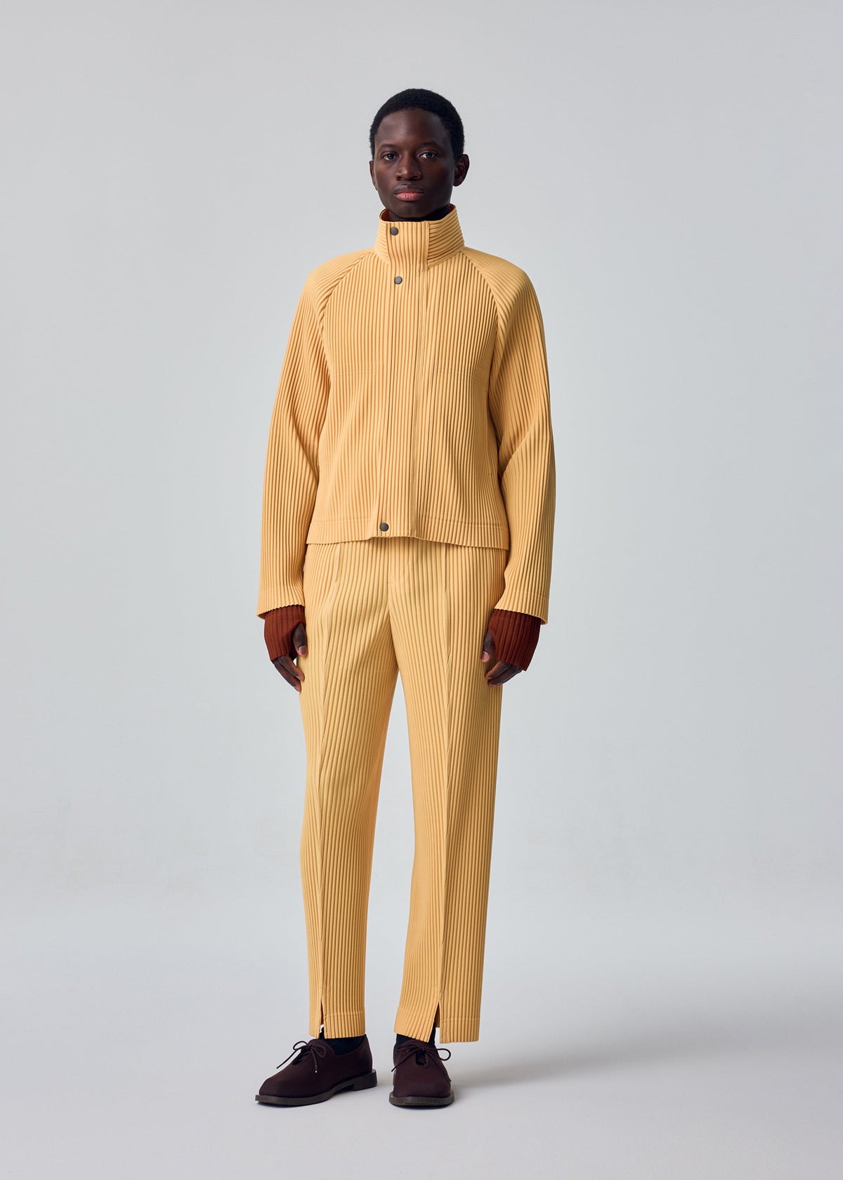 A model wears the HOMME PLISSÉ ISSEY MIYAKE TAILORED PLEATS 1 tailored-pleats-1-trousers-glow-orange-1.