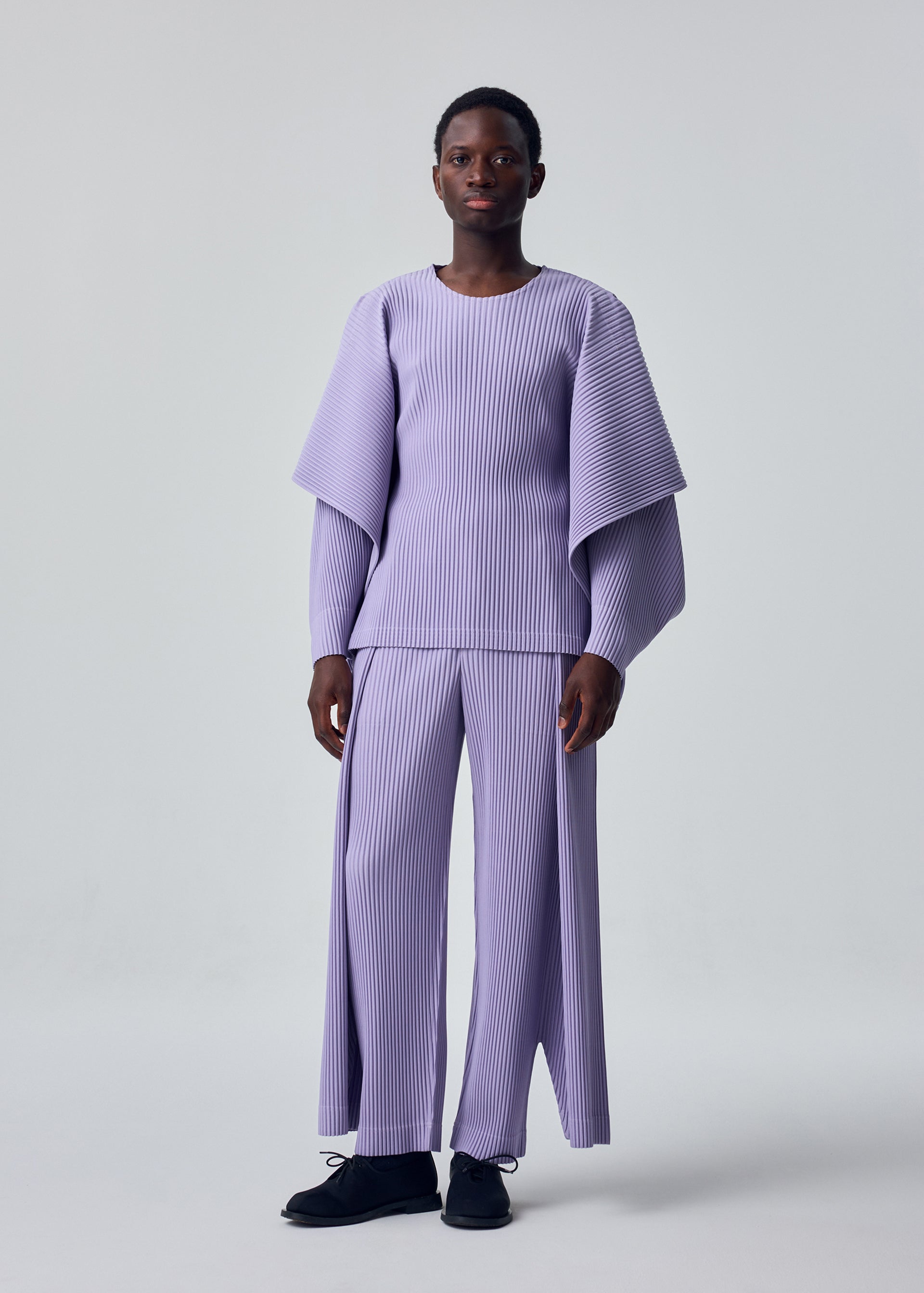 A model wears the HOMME PLISSÉ ISSEY MIYAKE MOTION BLUR motion-blur-trousers-darkside-brown-1.