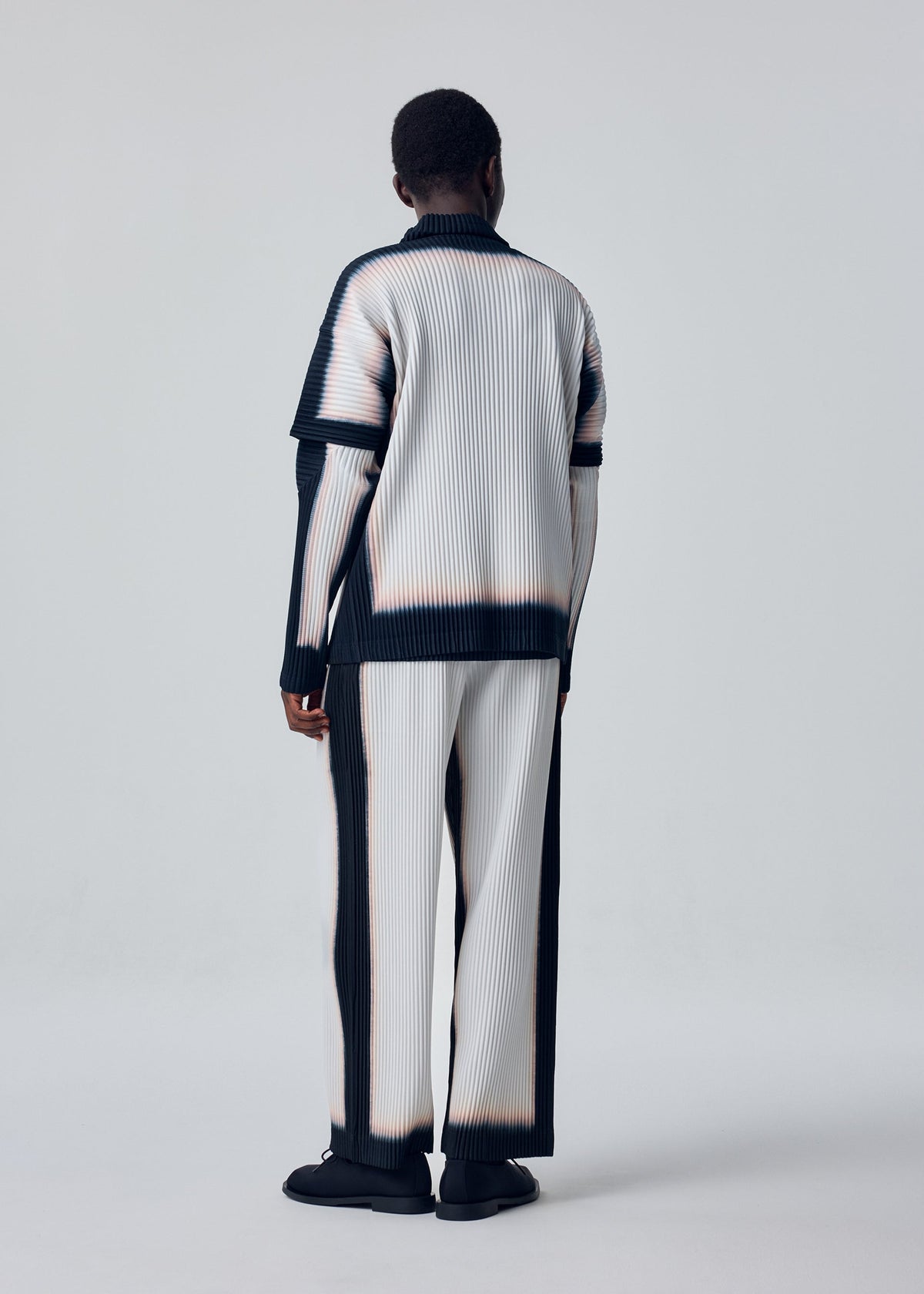 A model wears the HOMME PLISSÉ ISSEY MIYAKE FRAMEWORK : CHUSEN trousers.