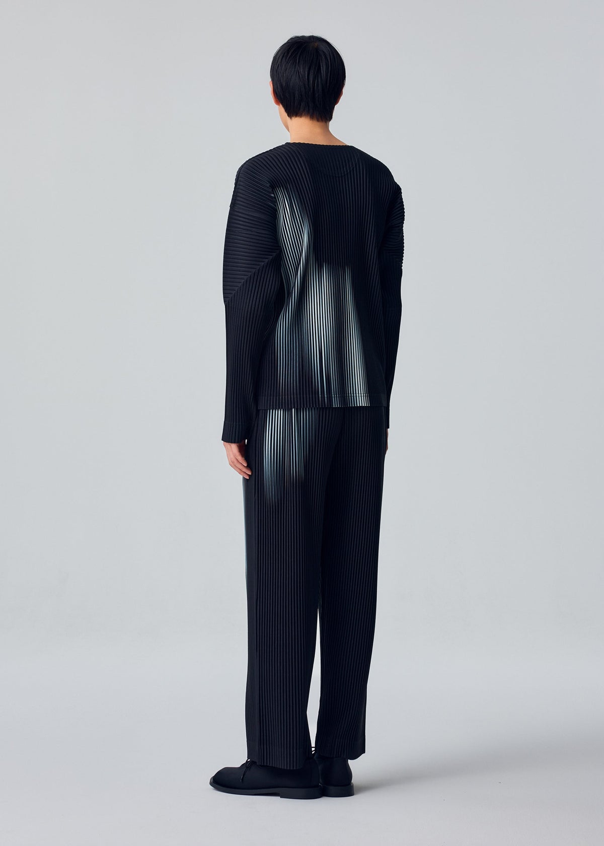A model wears the HOMME PLISSÉ ISSEY MIYAKE IN THE SHADOW trousers.