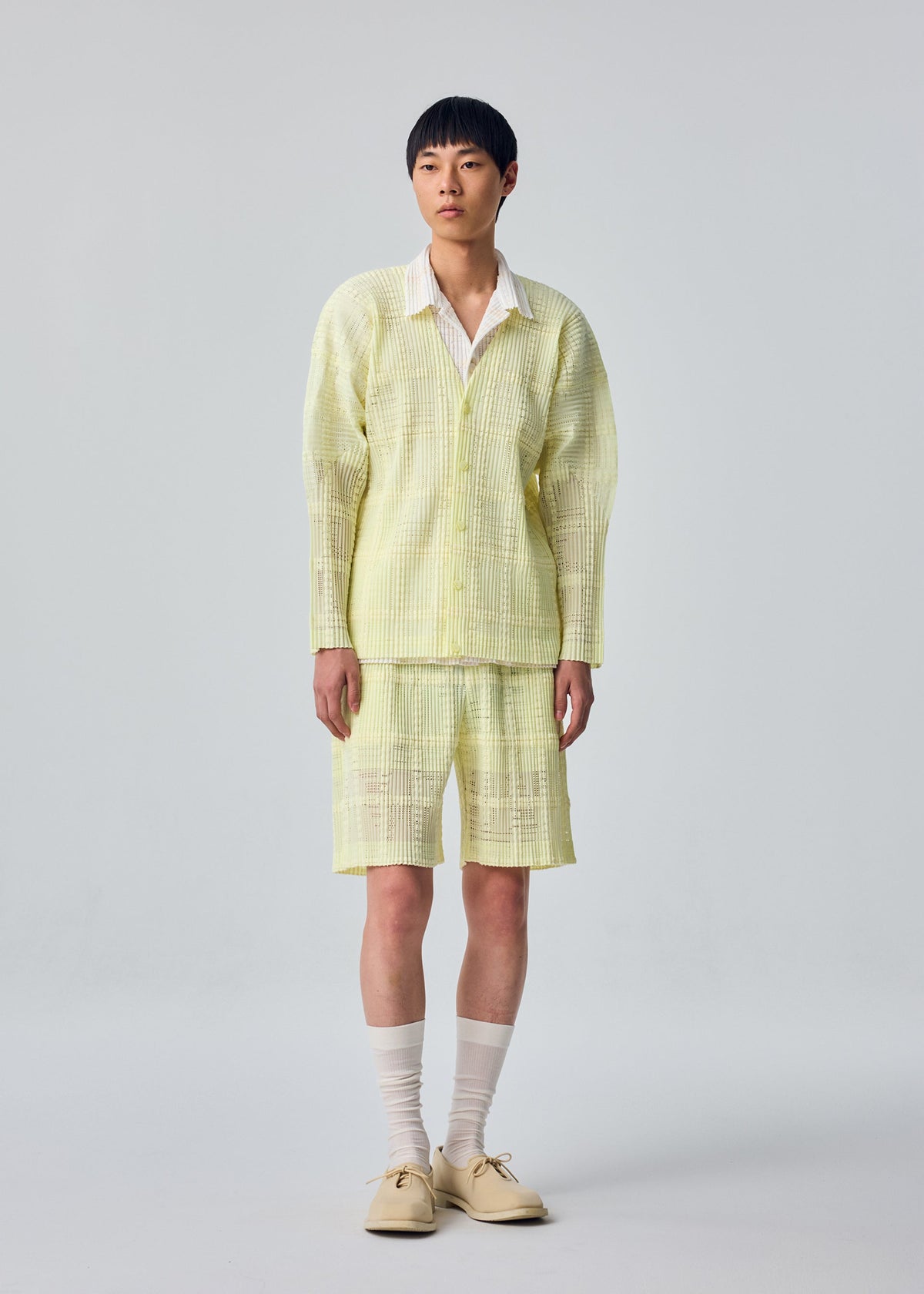 A model wears the HOMME PLISSÉ ISSEY MIYAKE LACE GRID PLEATS lace-grid-pleats-blouson-black.