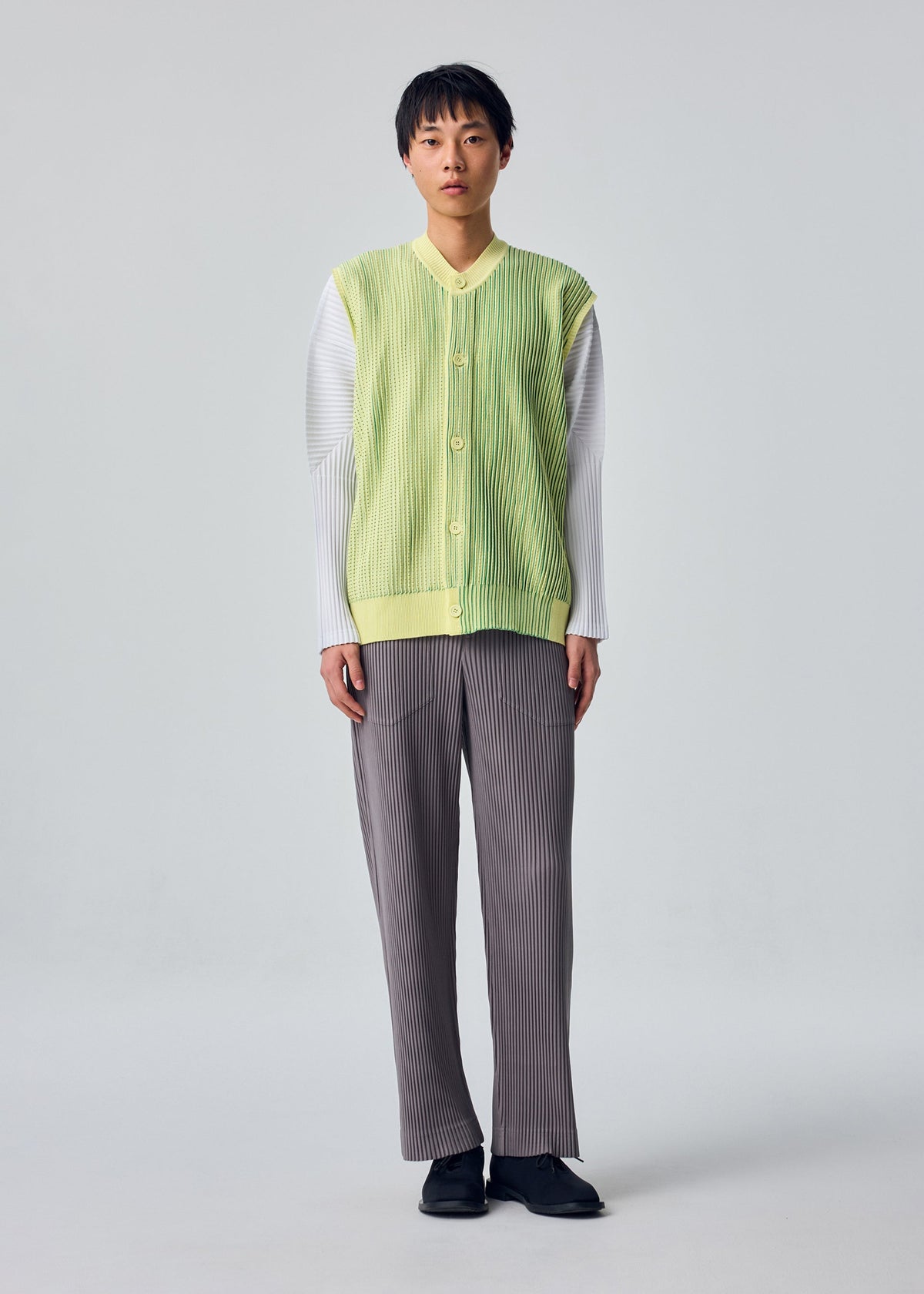 A model wears the HOMME PLISSÉ ISSEY MIYAKE IN THE SHADOW KNIT cardigan.