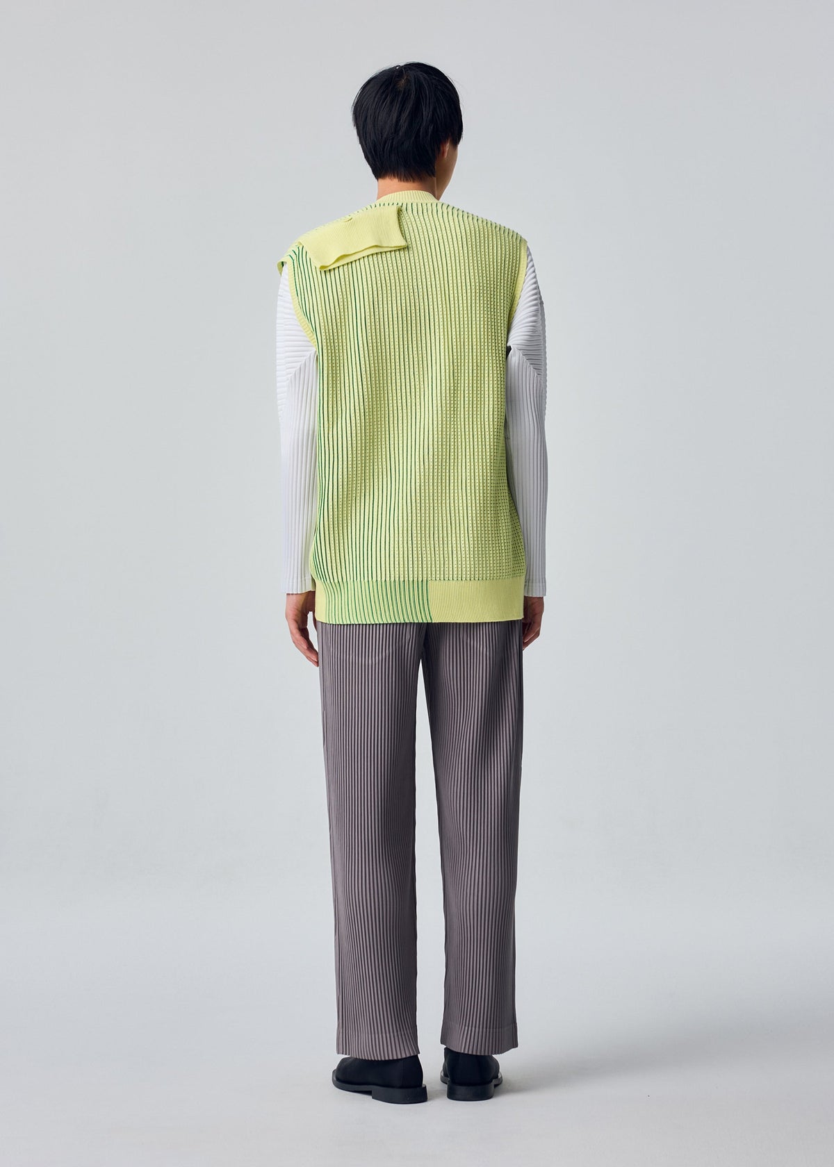 A model wears the HOMME PLISSÉ ISSEY MIYAKE IN THE SHADOW KNIT cardigan.