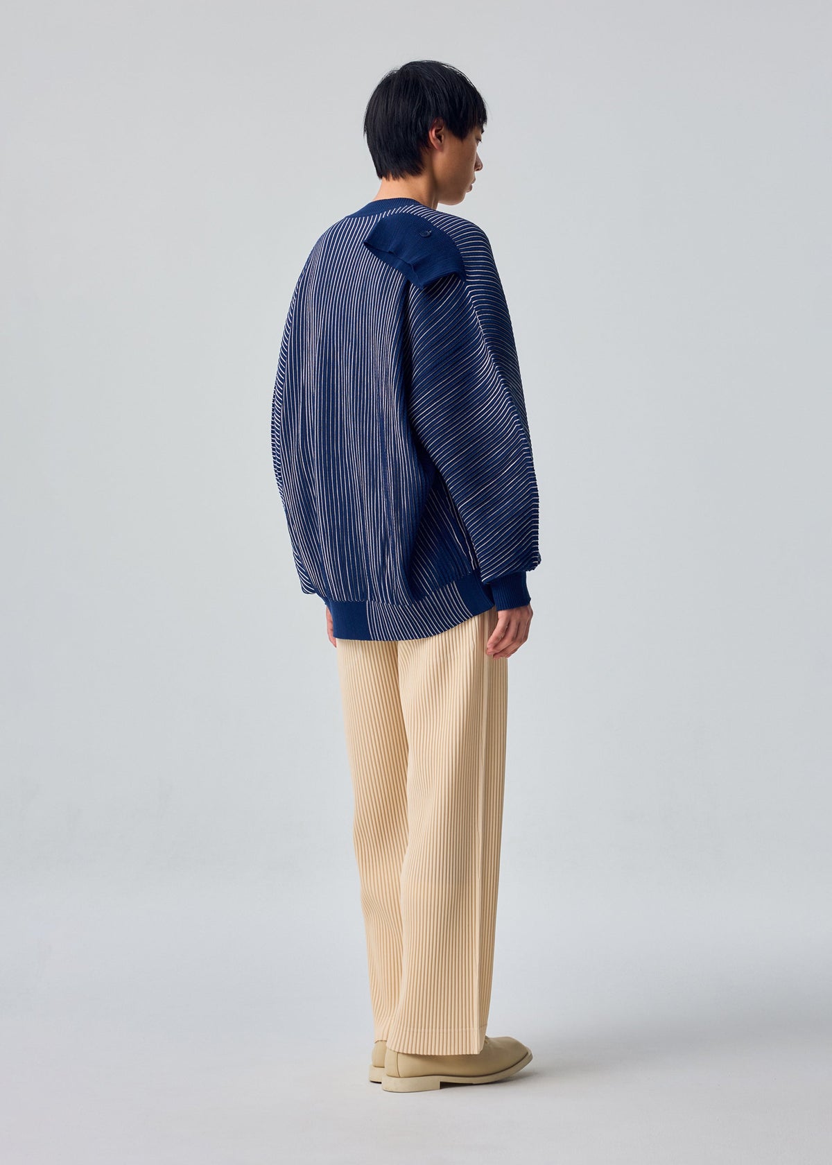 A model wears the HOMME PLISSÉ ISSEY MIYAKE IN THE SHADOW KNIT knit.