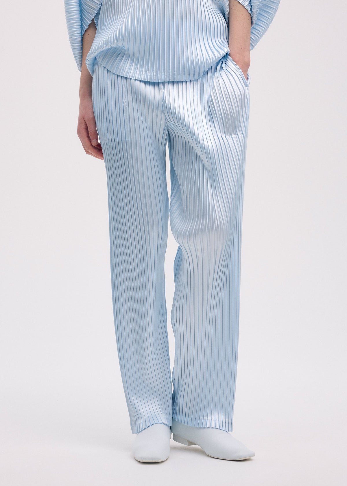 A model wears the Issey Miyake GLOSSED METAL PLEATS trousers.