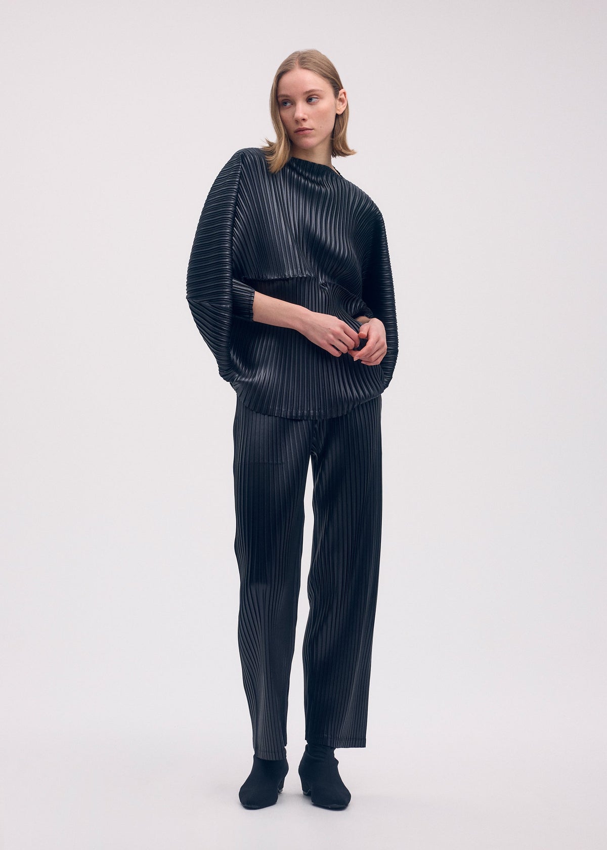 A model wears the Issey Miyake GLOSSED METAL PLEATS trousers.