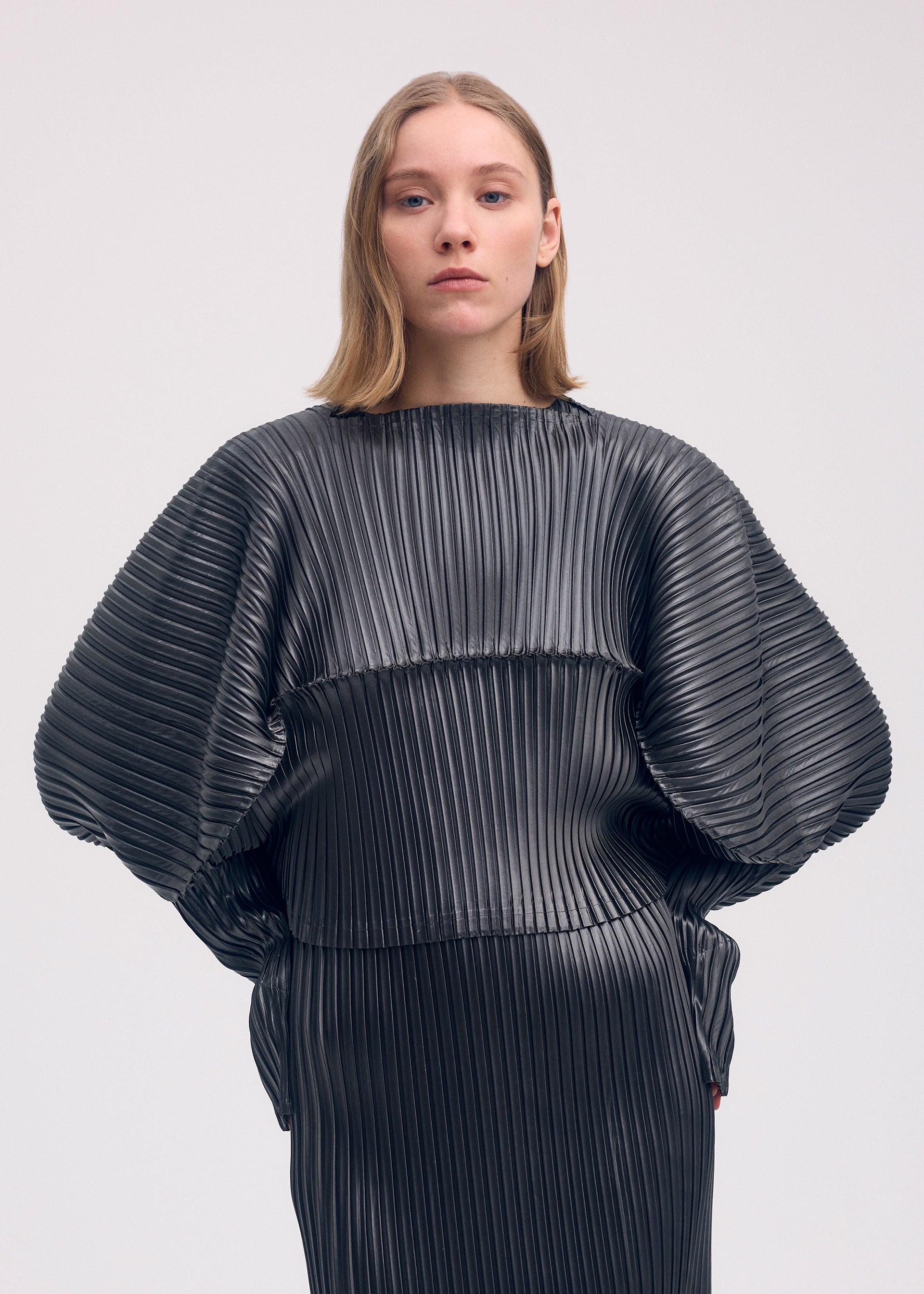 A model wears the Issey Miyake GLOSSED METAL PLEATS shirt.