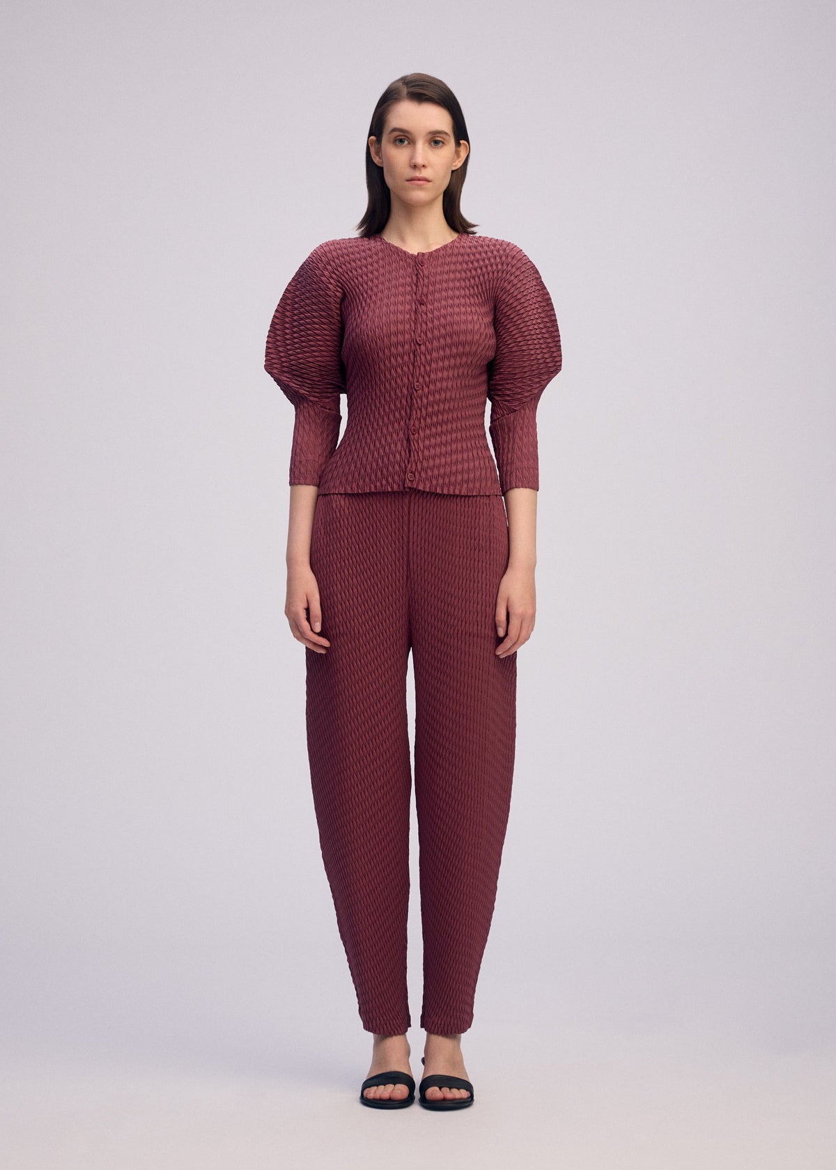A model wears the ISSEY MIYAKE SLEEK PLEATS sleek-pleats-cardigan-light-grey.