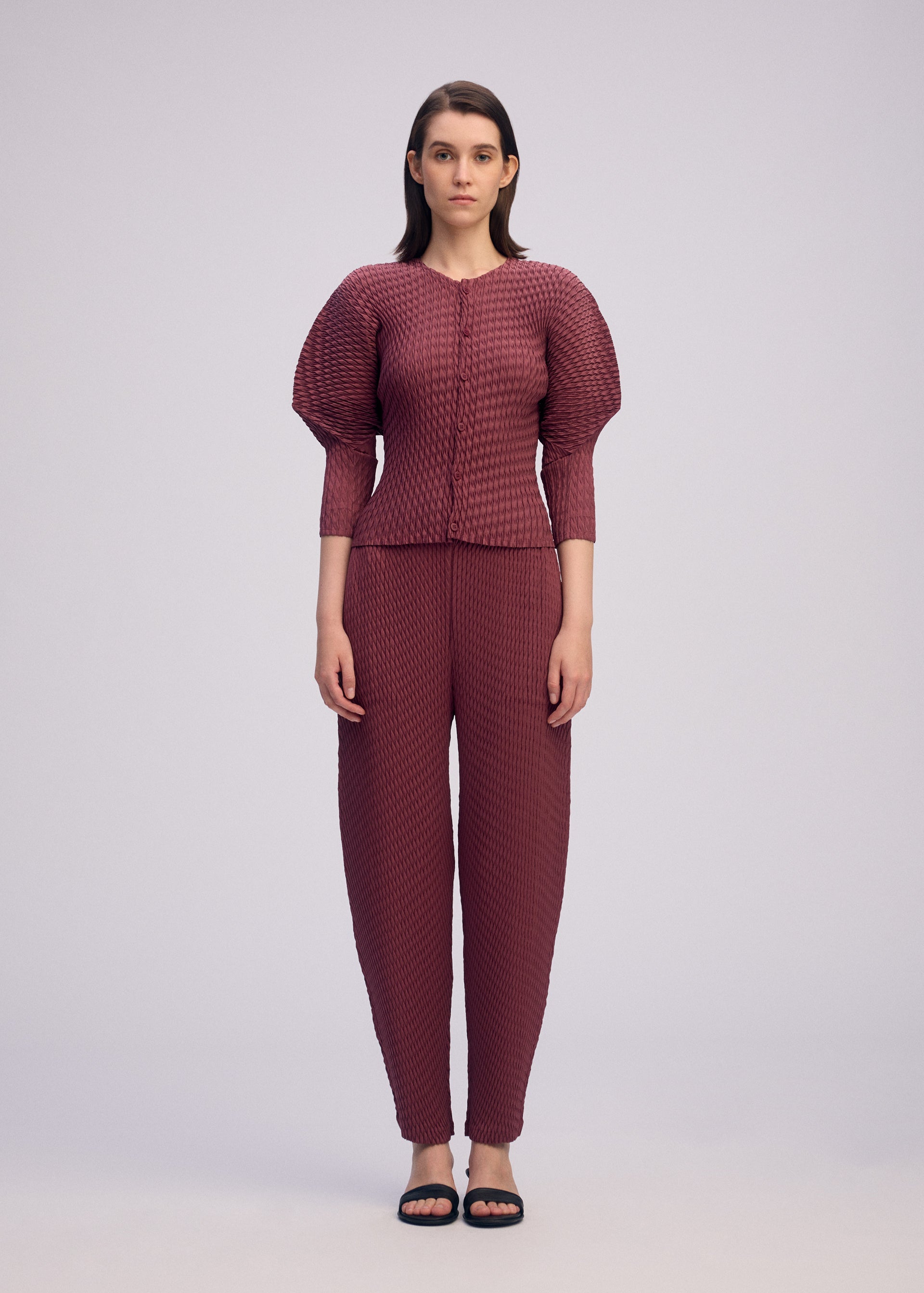 A model wears the ISSEY MIYAKE SLEEK PLEATS sleek-pleats-cardigan-light-grey.