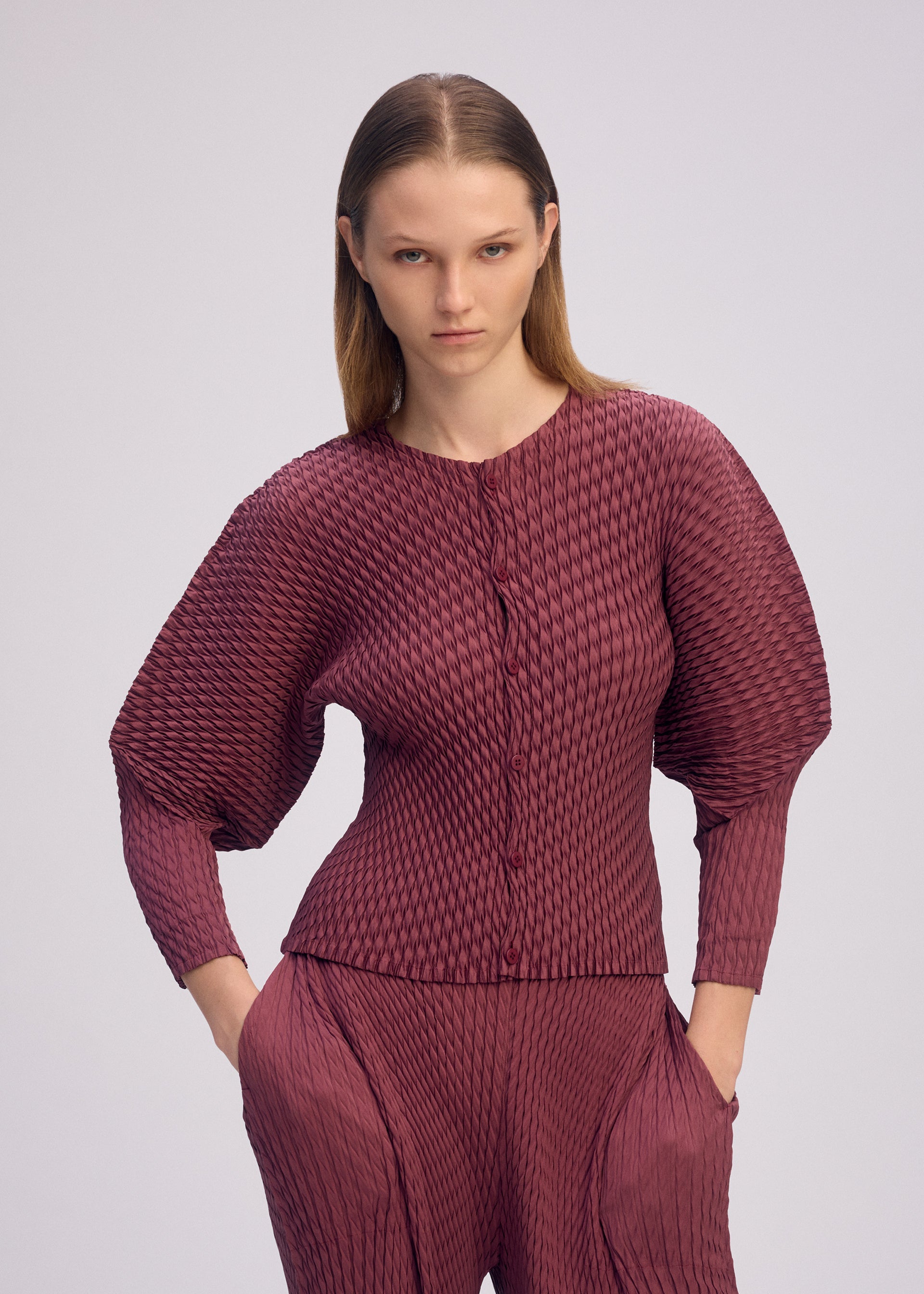 A model wears the ISSEY MIYAKE SLEEK PLEATS sleek-pleats-cardigan-burgundy.