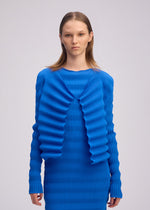 A model wears the ISSEY MIYAKE SPRING PLEATS spring-pleats-cardigan-chukar-beige.