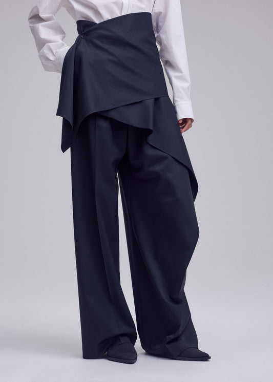 A model wears the ISSEY MIYAKE LUSTROUS WOOL PANTS trousers.