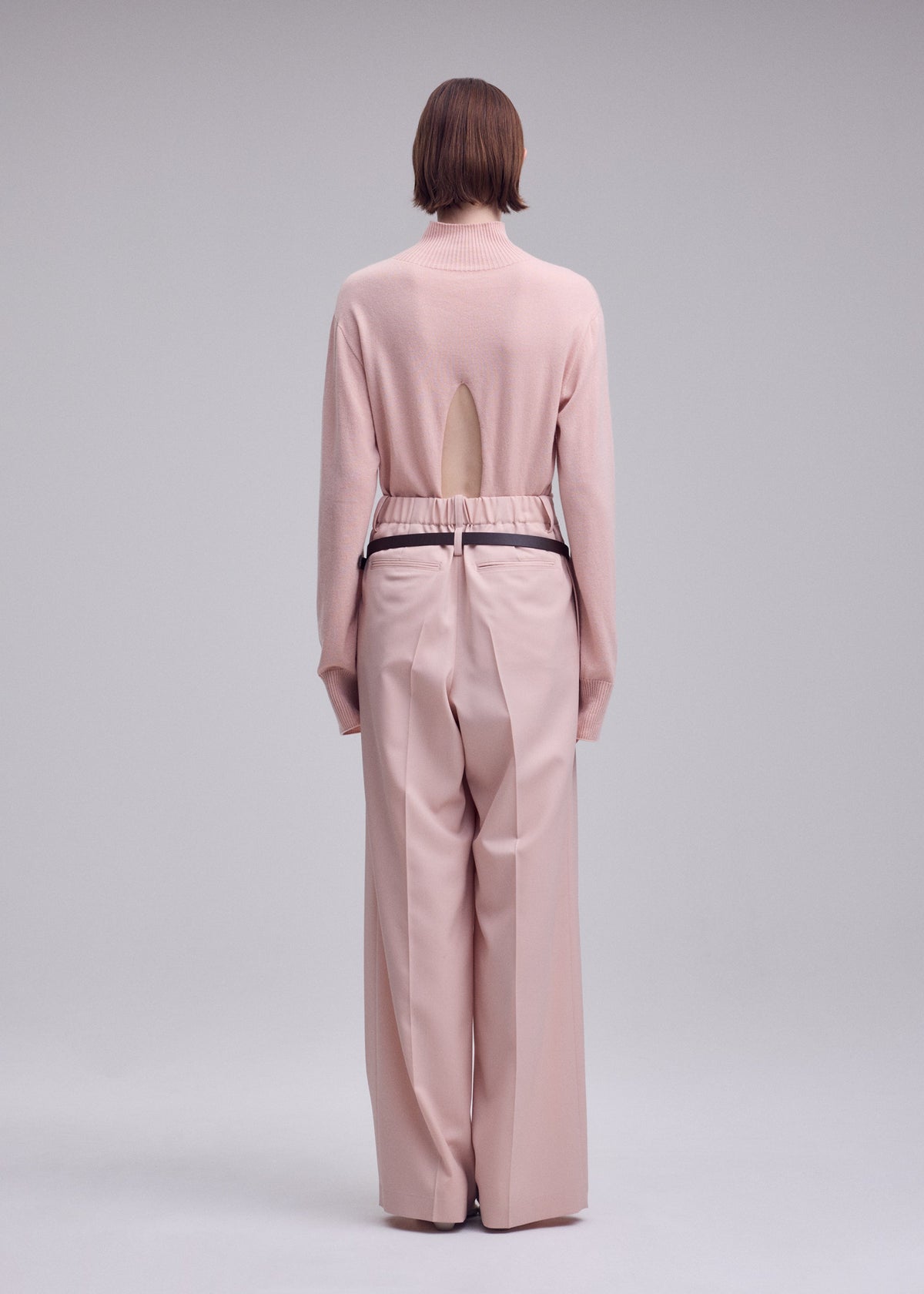 A model wears the ISSEY MIYAKE LUSTROUS WOOL PANTS trousers.