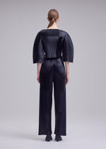A model wears the ISSEY MIYAKE GLOSSED PANELS PLEATS trousers.