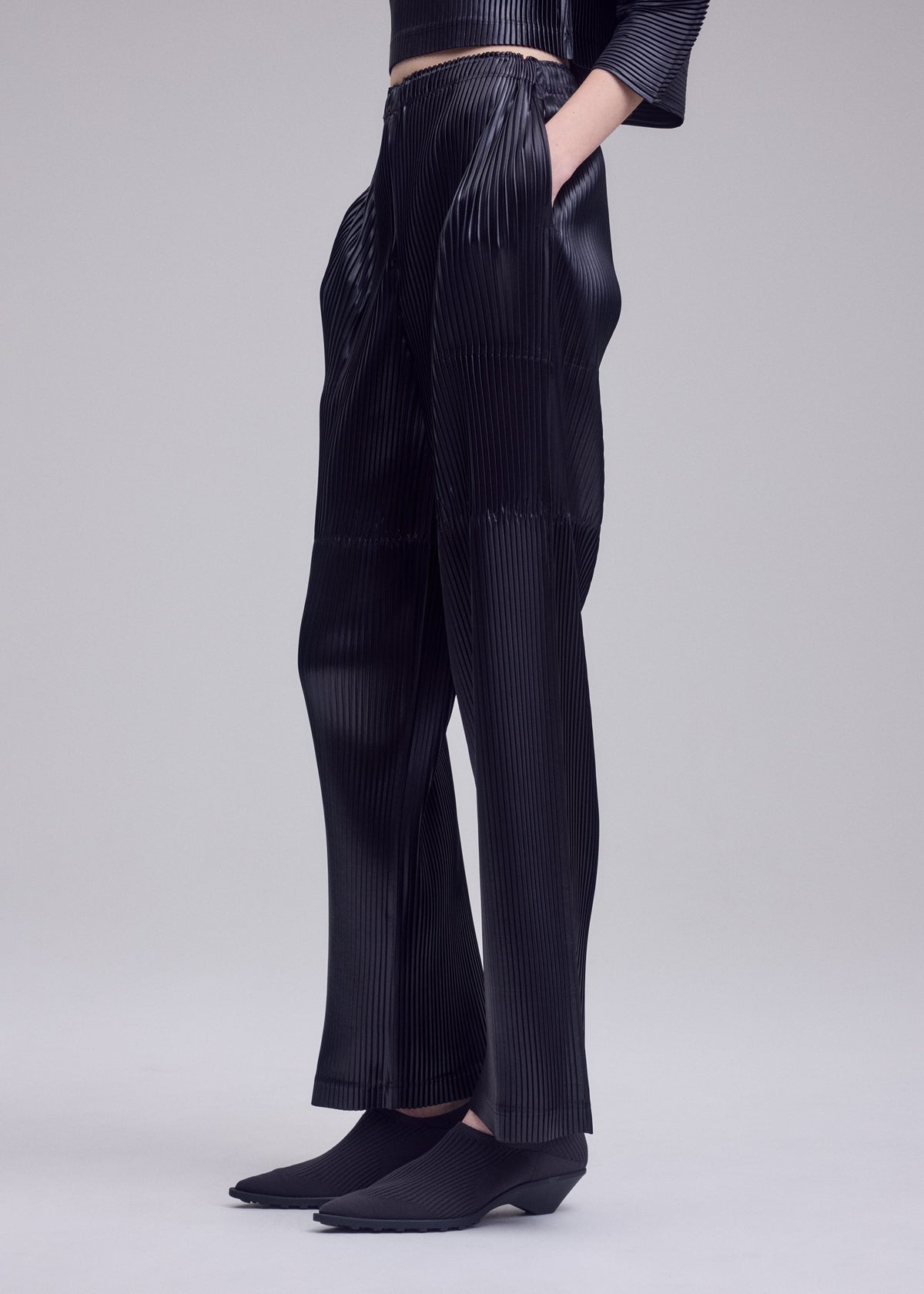 A model wears the ISSEY MIYAKE GLOSSED PANELS PLEATS trousers.
