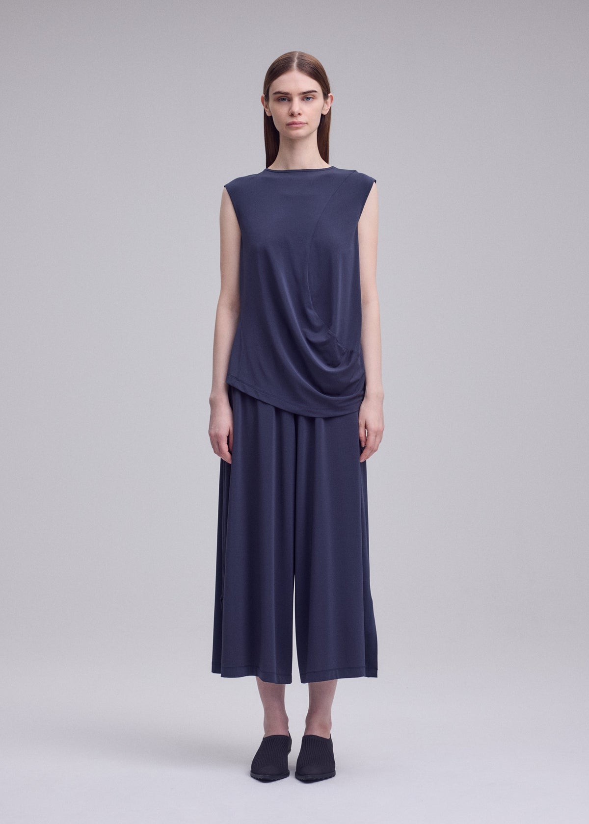 A model wears the ISSEY MIYAKE DRAPE JERSEY-68 drape-jersey-68-trousers-dark-navy-2.