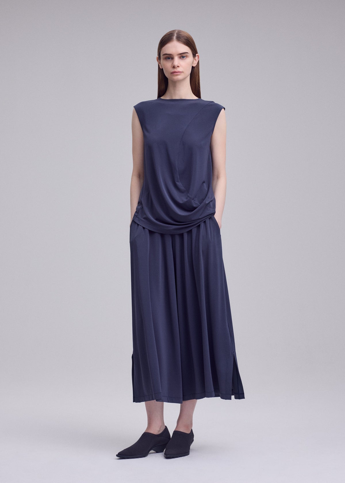 A model wears the ISSEY MIYAKE DRAPE JERSEY-68 drape-jersey-68-trousers-off-white.