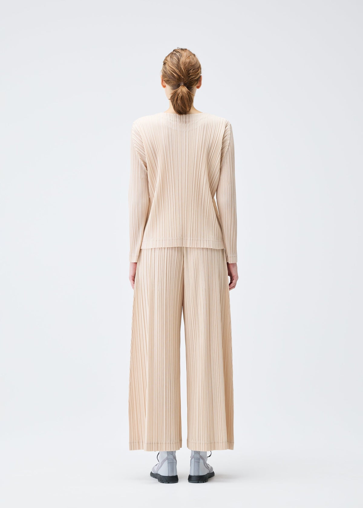 A model wears the Pleats Please Issey Miyake WOOL PLEATS trousers.