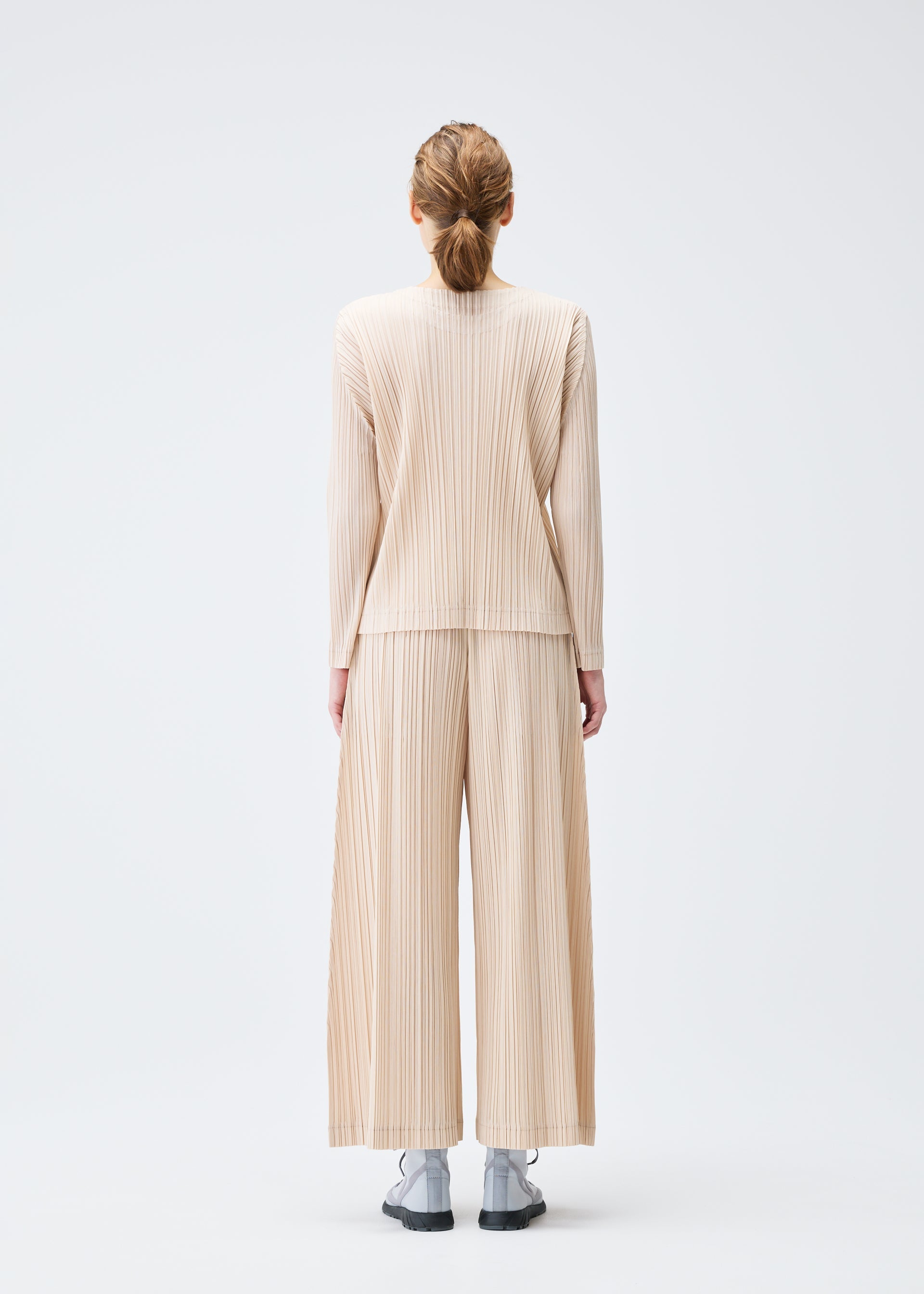A model wears the Pleats Please Issey Miyake WOOL PLEATS trousers.