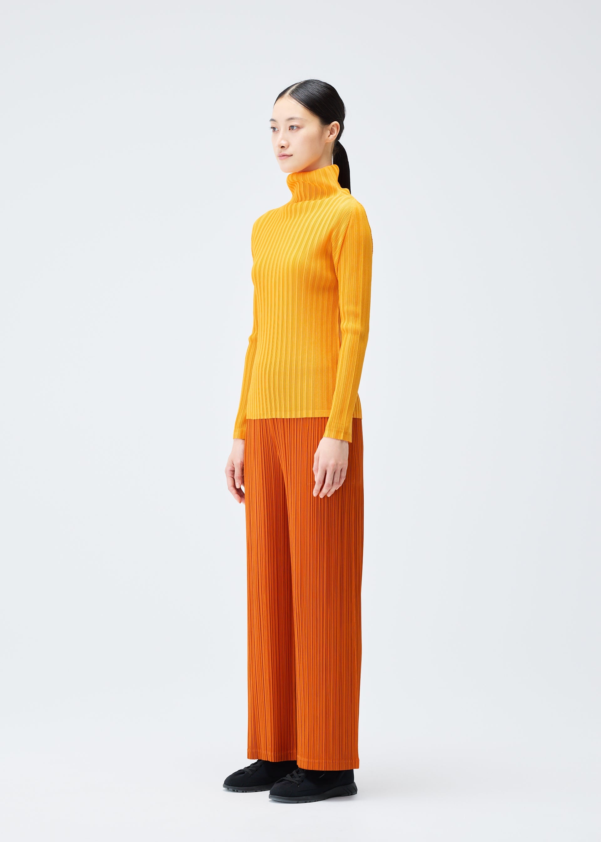 A model wears the Pleats Please Issey Miyake LOOP BOTTOMS trousers.